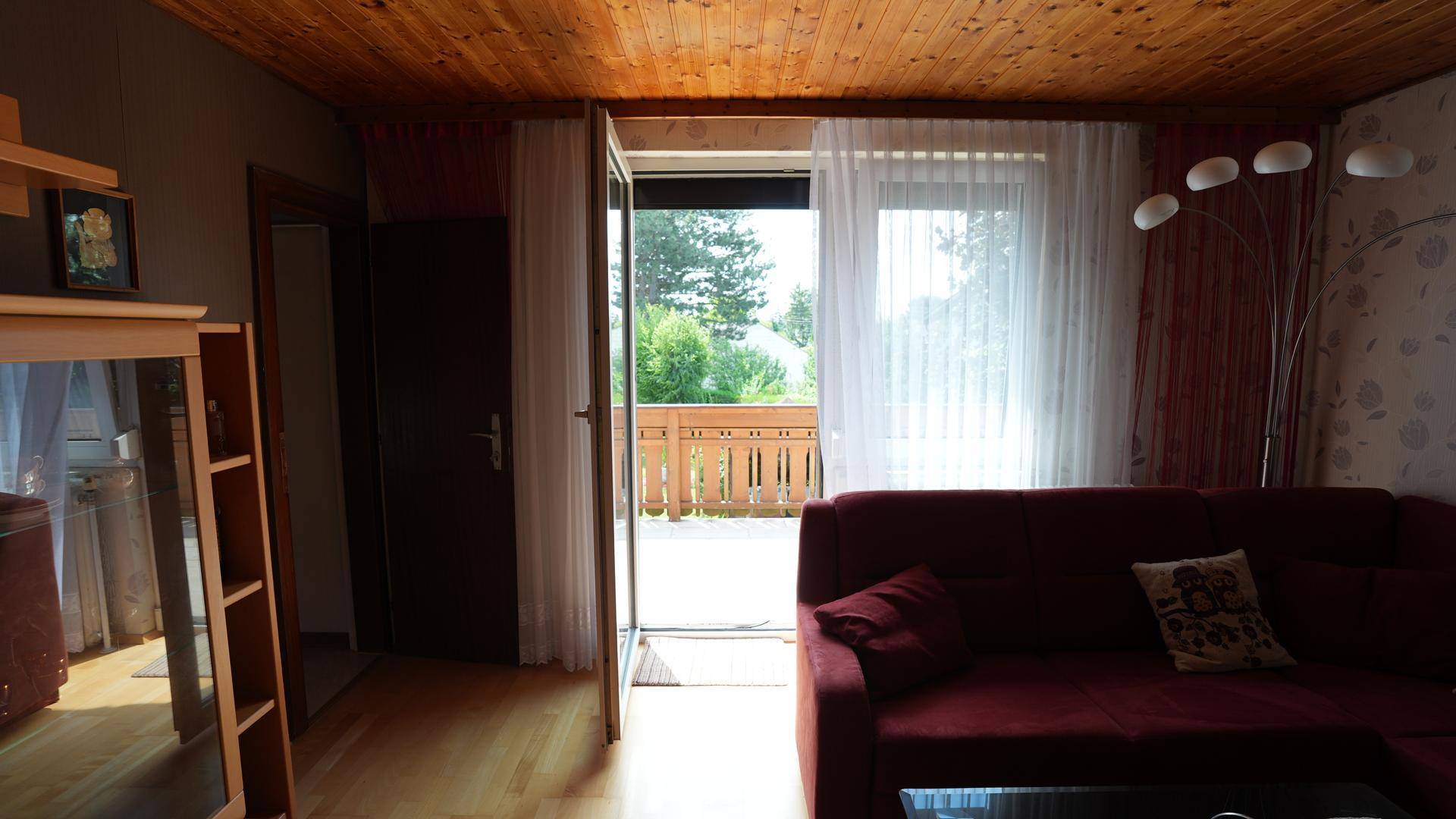 Helles Wohnzimmer mit Holzboden, Holzdecke und Zugang zu einem sonnigen Balkon.