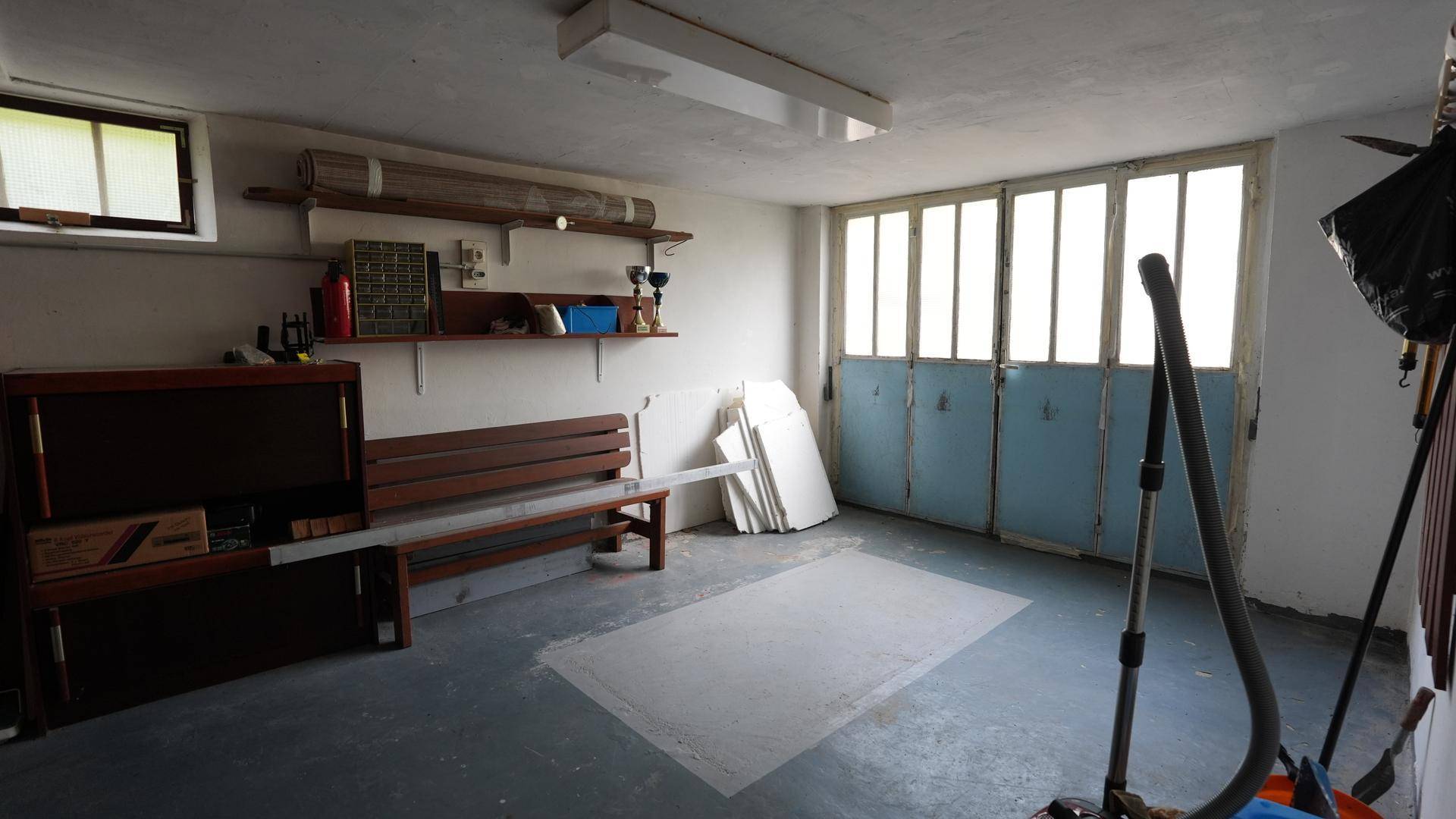 Geräumige Garage mit Betonboden, Fenstern und vielseitigem Stauraum für Werkzeuge und Geräte.