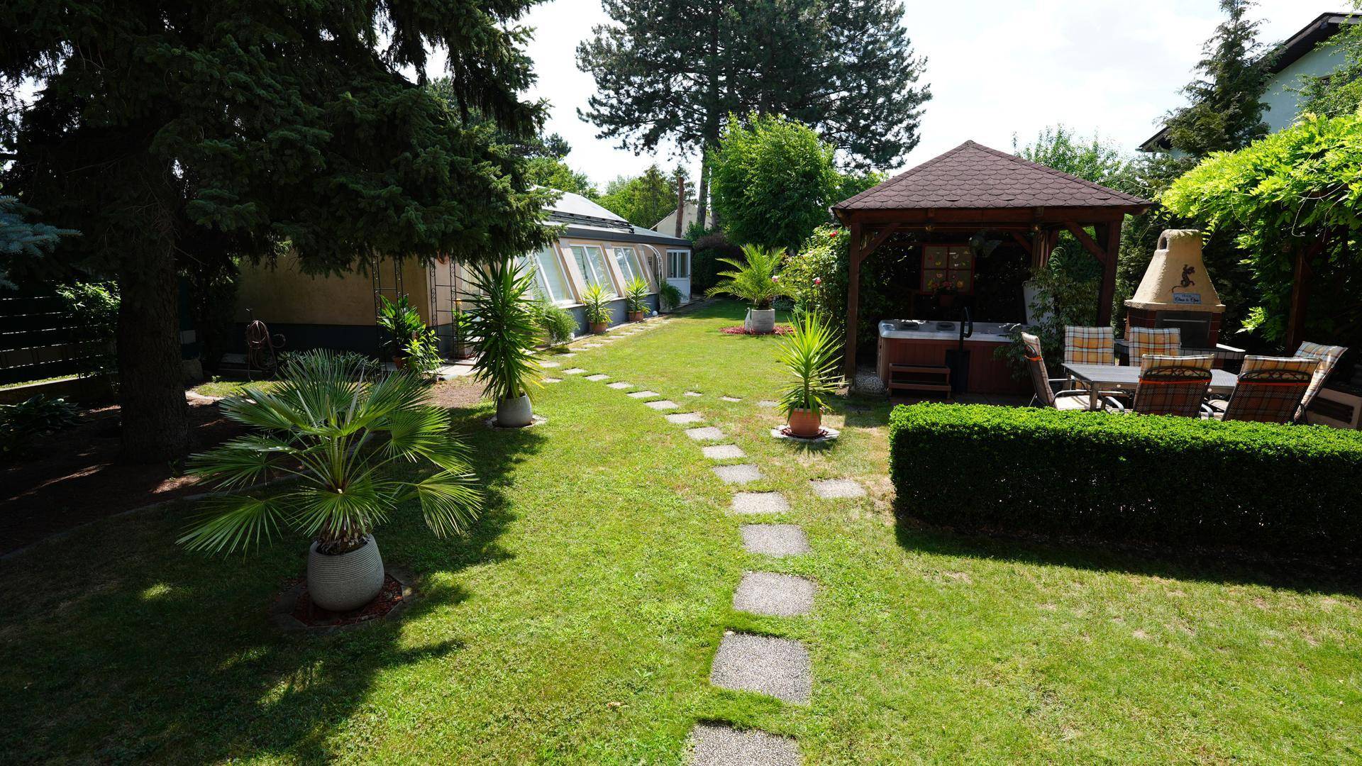 Weitläufiger Garten mit Rasen, Steinpfad, Palmen und einem Pavillon mit Whirlpool und Essbereich.