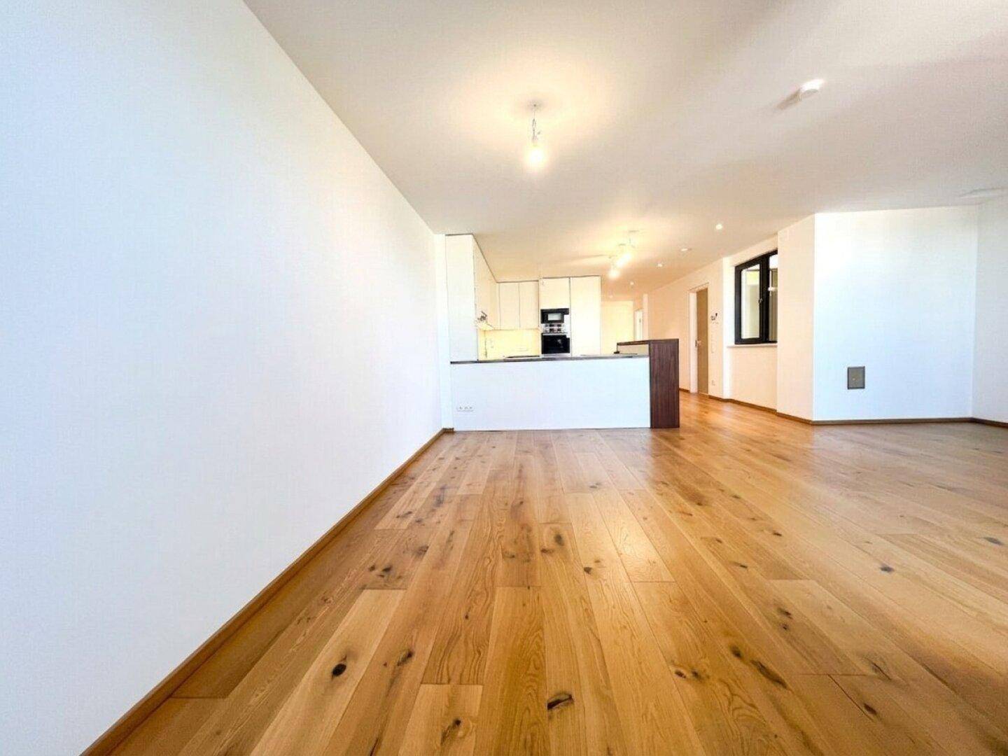 Geräumiger offener Wohnbereich mit hellem Holzboden und Blick auf die moderne Küche.