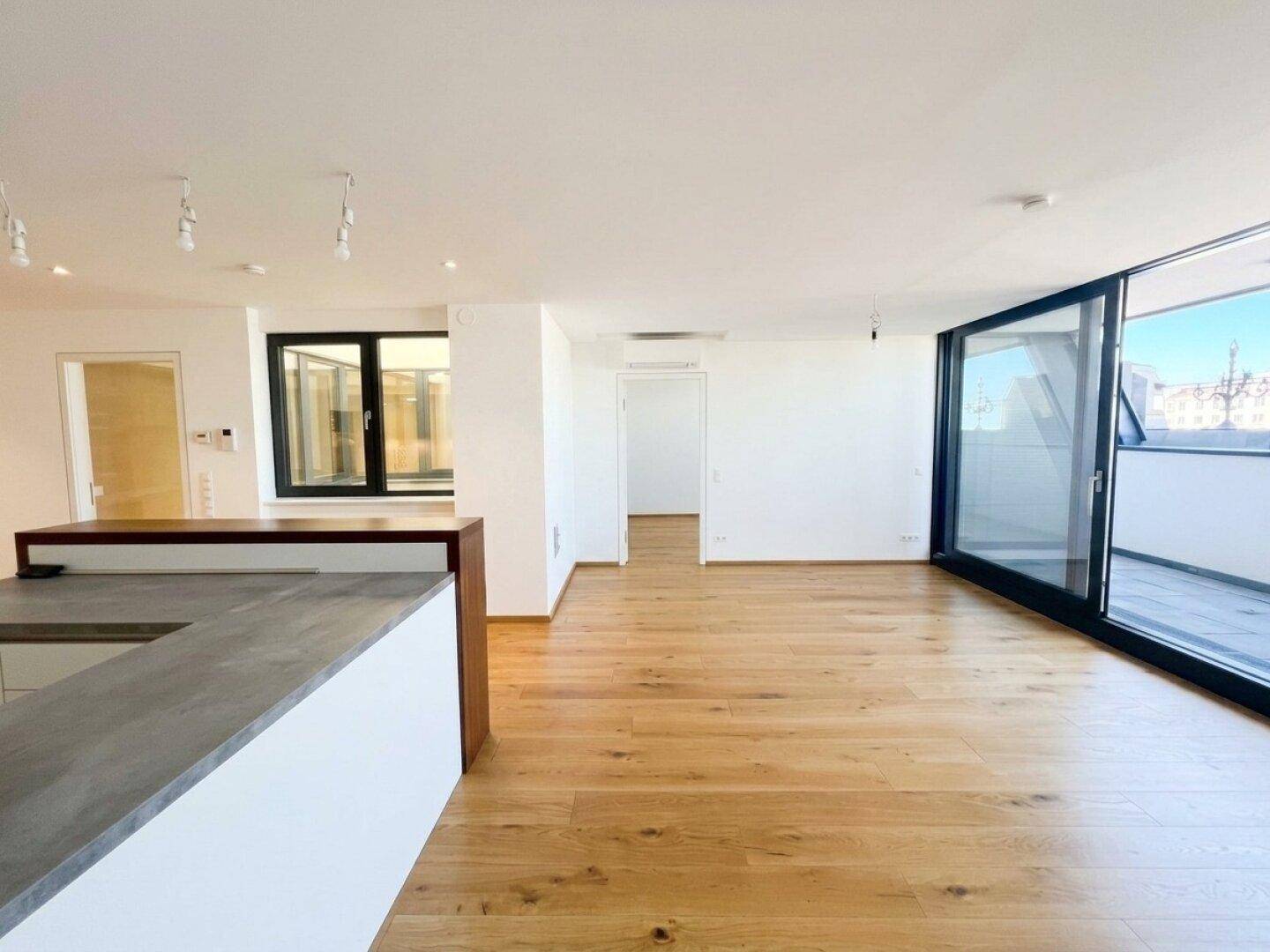 Weitläufiger Wohnbereich mit Holzboden, Küchenzeile und großzügigen Fensterfronten.