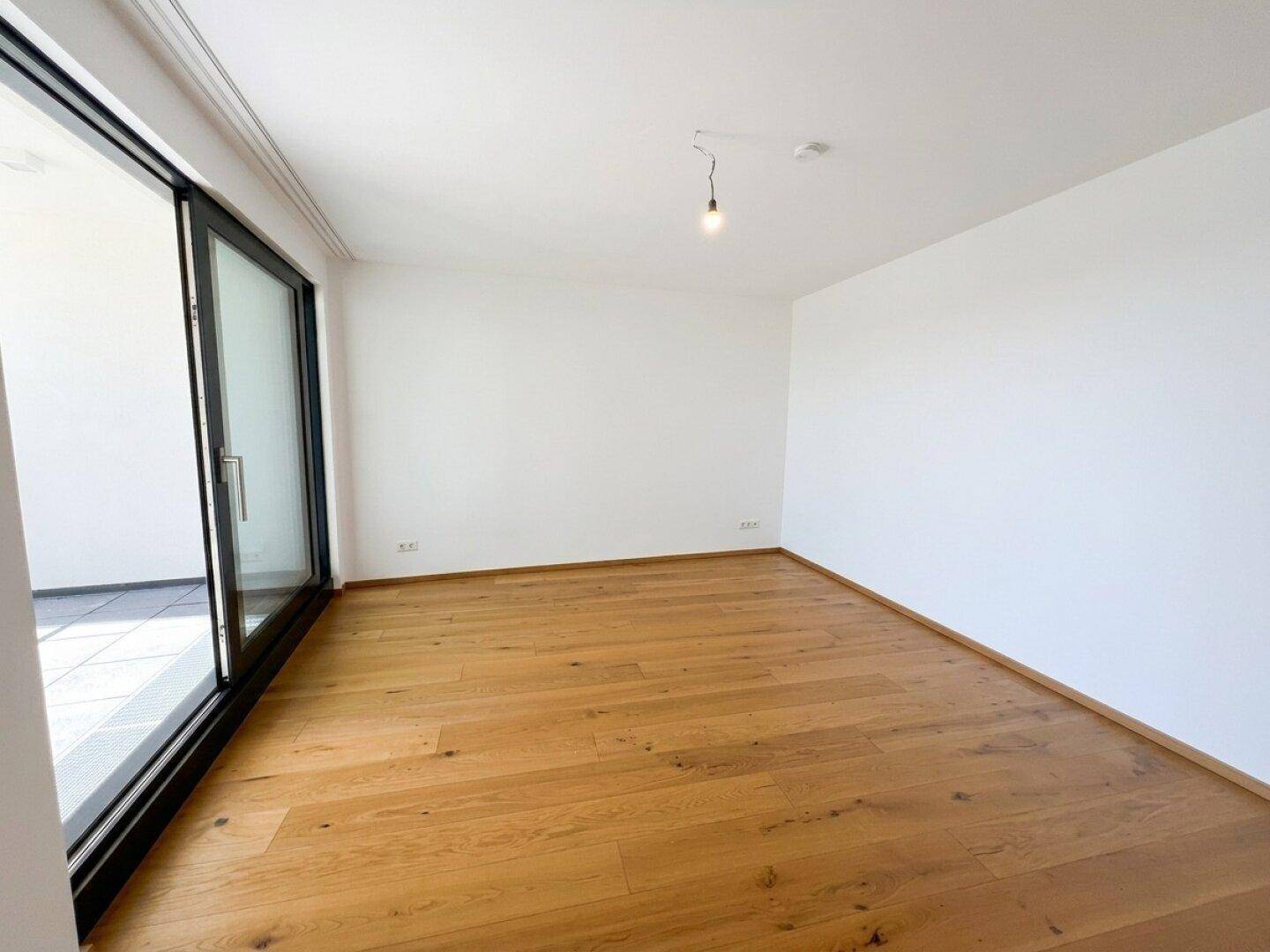 Geräumiges Zimmer mit Holzboden und großer Schiebetür, ideal als Schlafzimmer nutzbar.