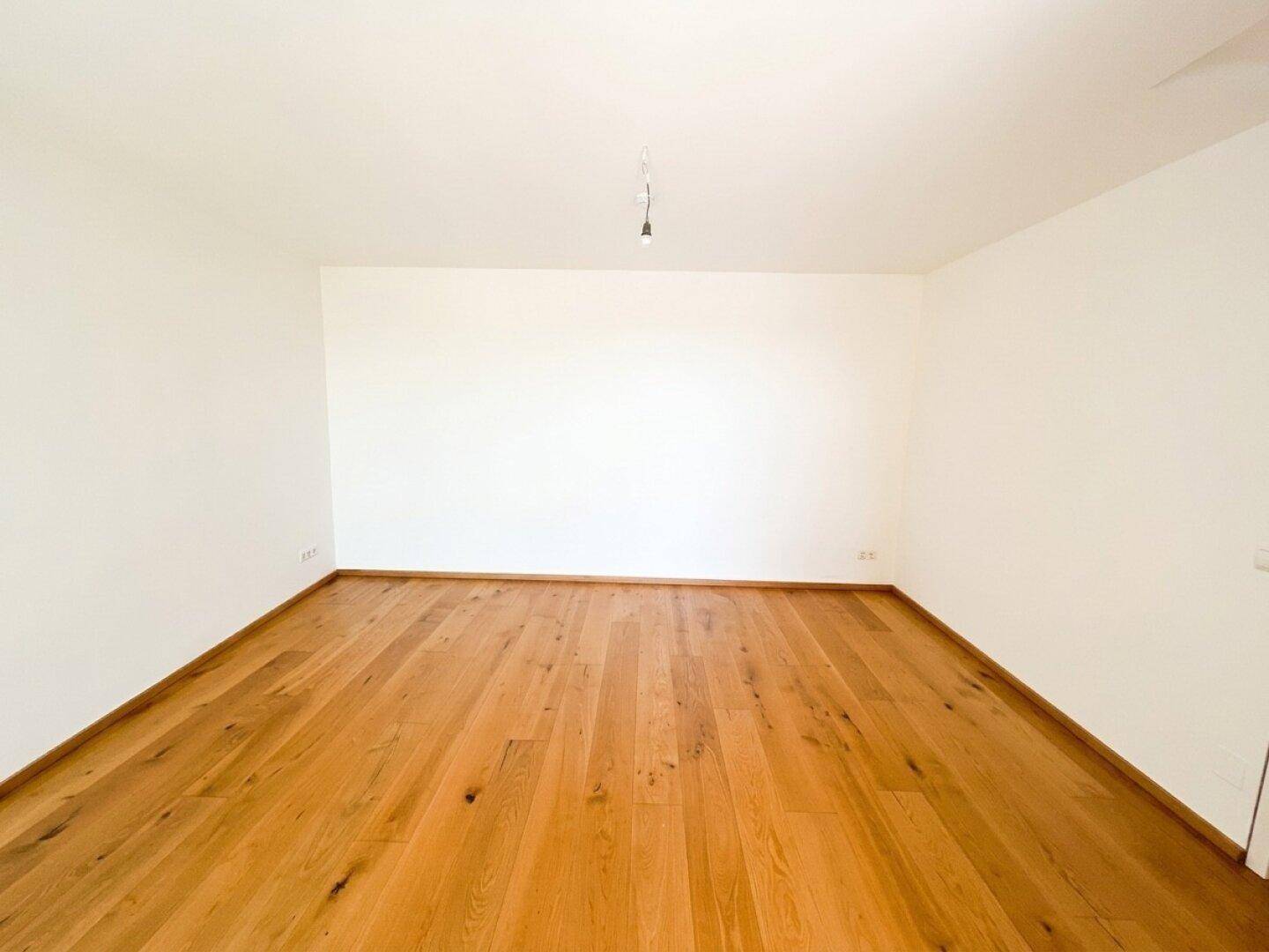 Leeres Zimmer mit hellem Holzboden und weißen Wänden, vielseitig nutzbar.