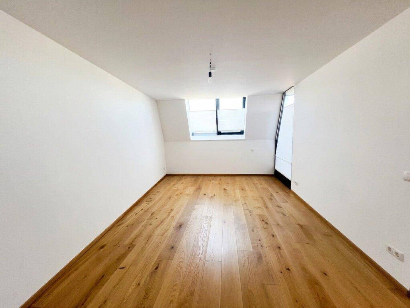 Helles Zimmer mit Holzboden, Dachschräge und Fenster, ideal als Schlafzimmer.