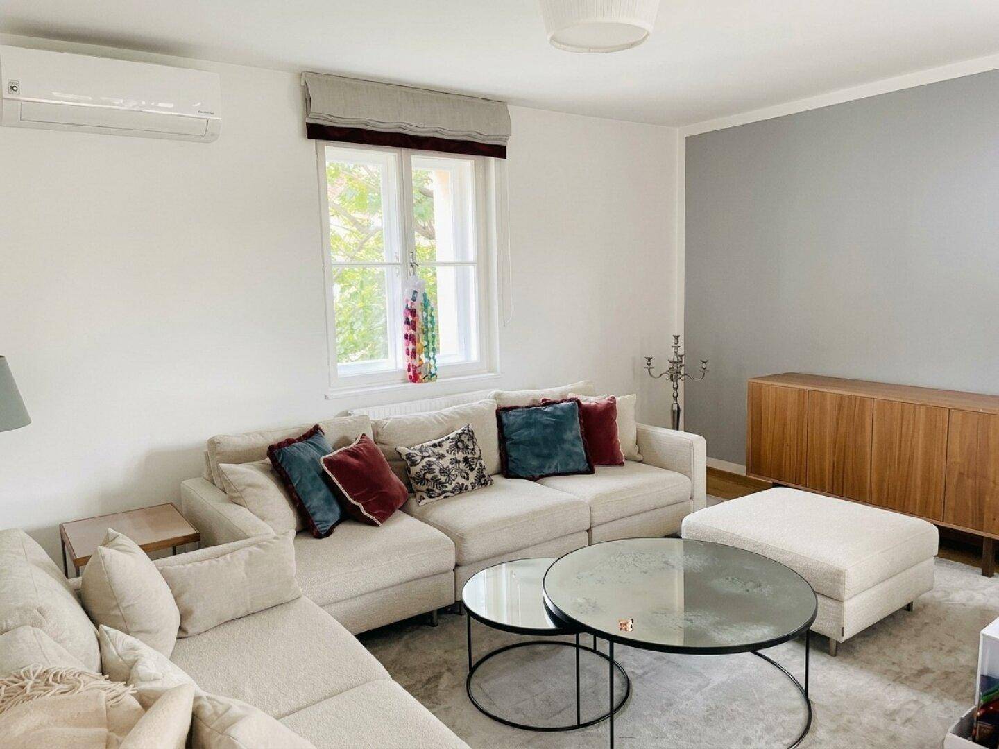 Gemütliches Wohnzimmer mit beigem Sofa, Teppich und Klimaanlage.