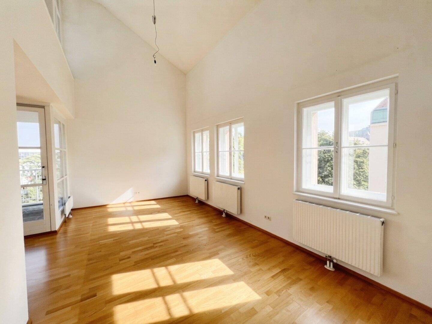 Lichtdurchfluteter Wohnraum mit hohen Decken, Parkettboden und großen Fenstern.