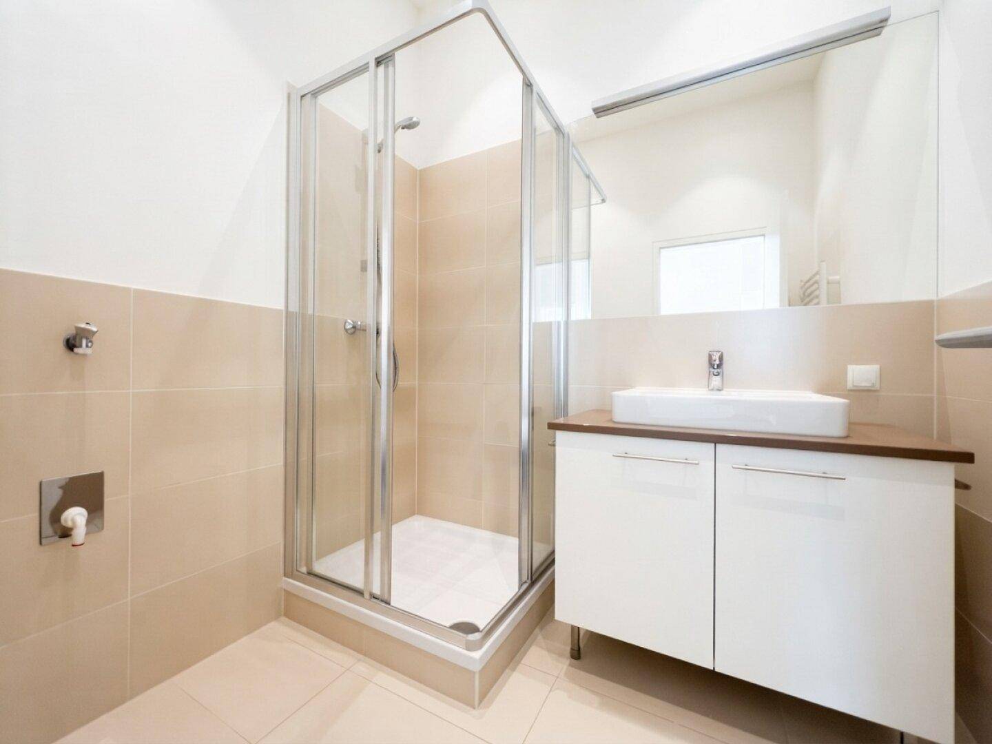 Modernes Badezimmer mit Duschkabine, Waschbecken und großem Spiegel, in hellen Beigetönen gefliest.