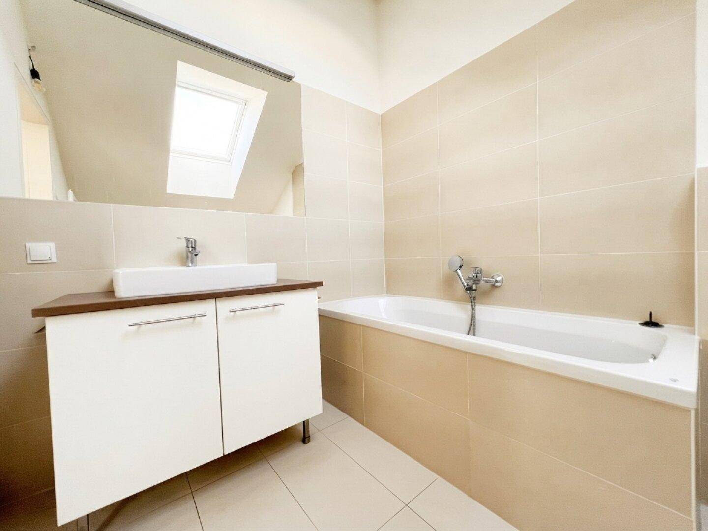 Modernes Badezimmer im Dachgeschoss mit Badewanne, Waschbecken und Dachfenster.