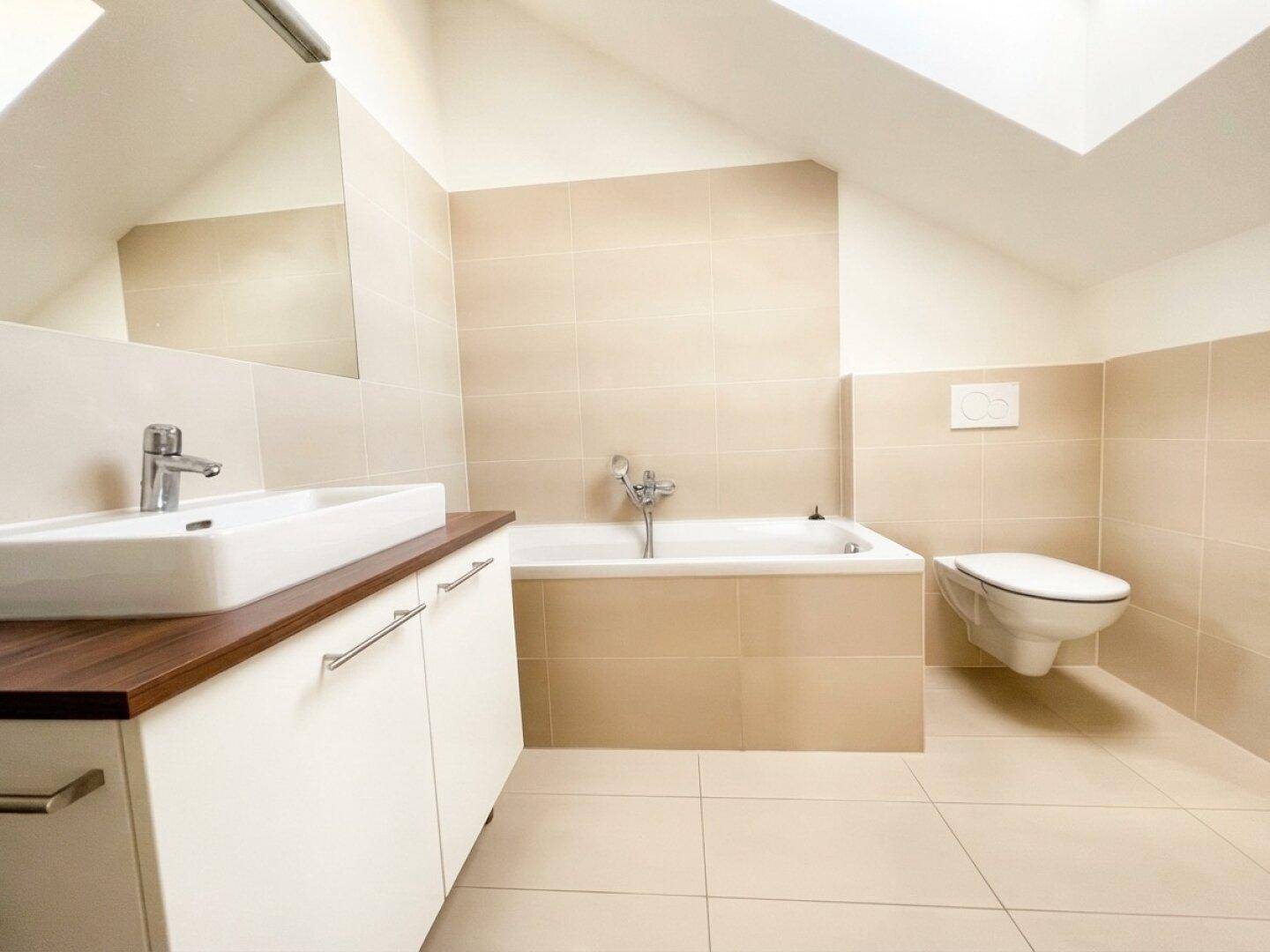 Helles Badezimmer im Dachgeschoss mit Badewanne, Waschbecken und WC, gefliest in beigen Farbtönen.