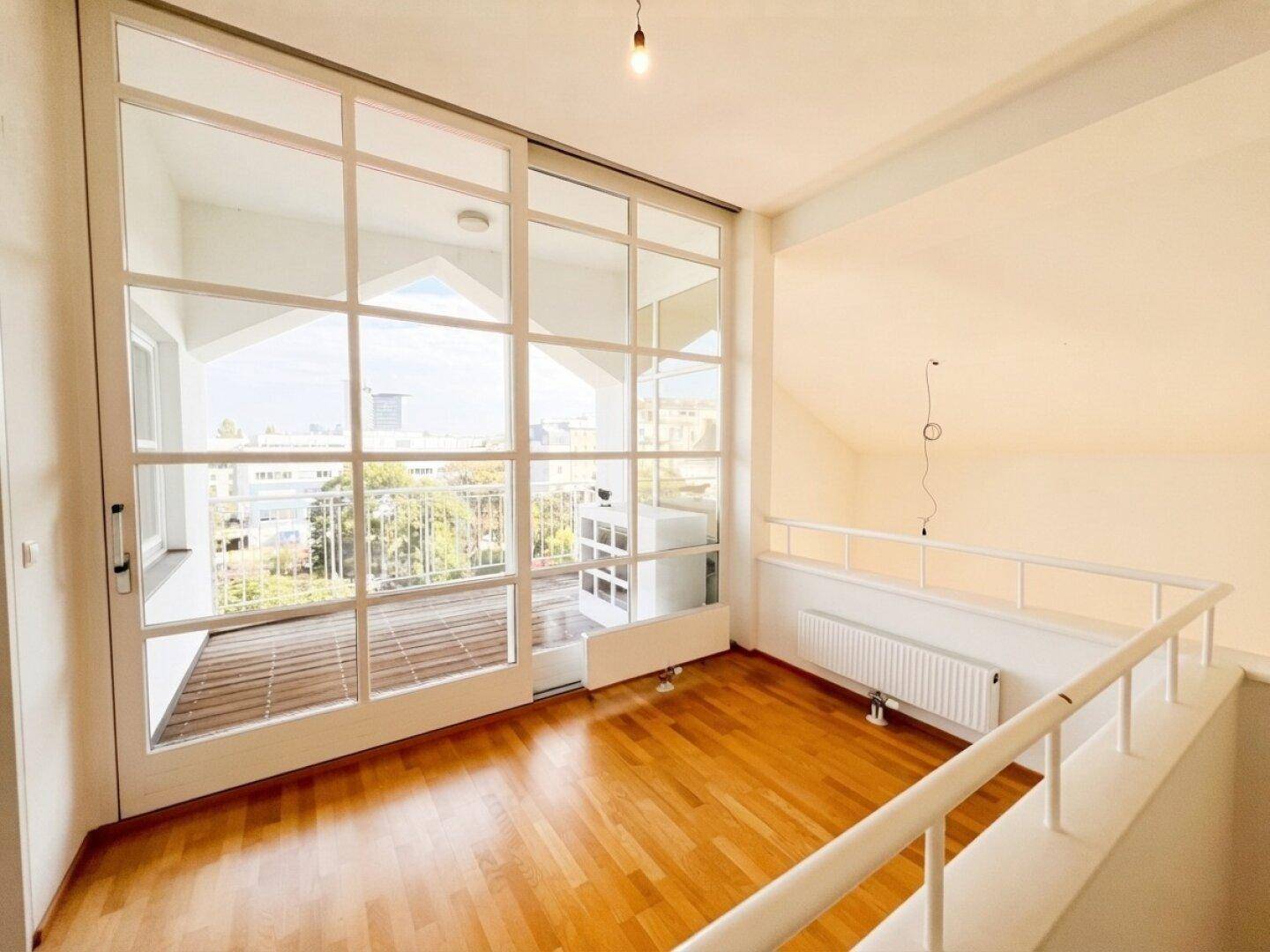 Heller Wohnbereich im Obergeschoss mit Parkettboden und großem Fenster zum Balkon.