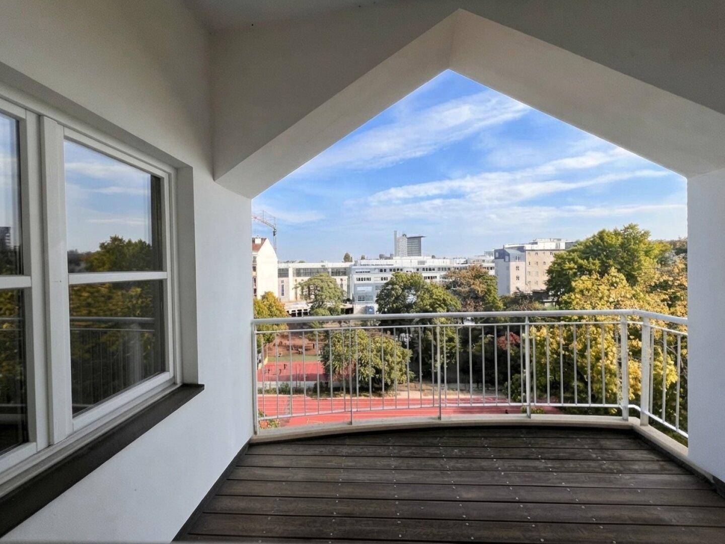 Balkon mit Holzboden und weitem Blick auf Sportanlagen und die Stadt.
