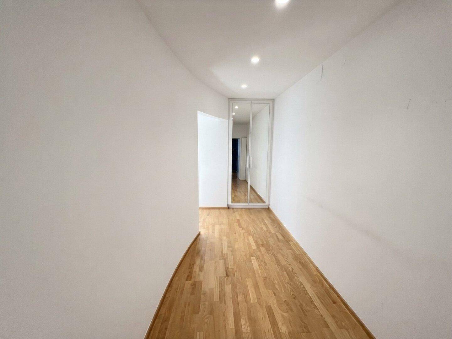Heller Flur mit Parkettboden und integriertem Spiegelschrank.