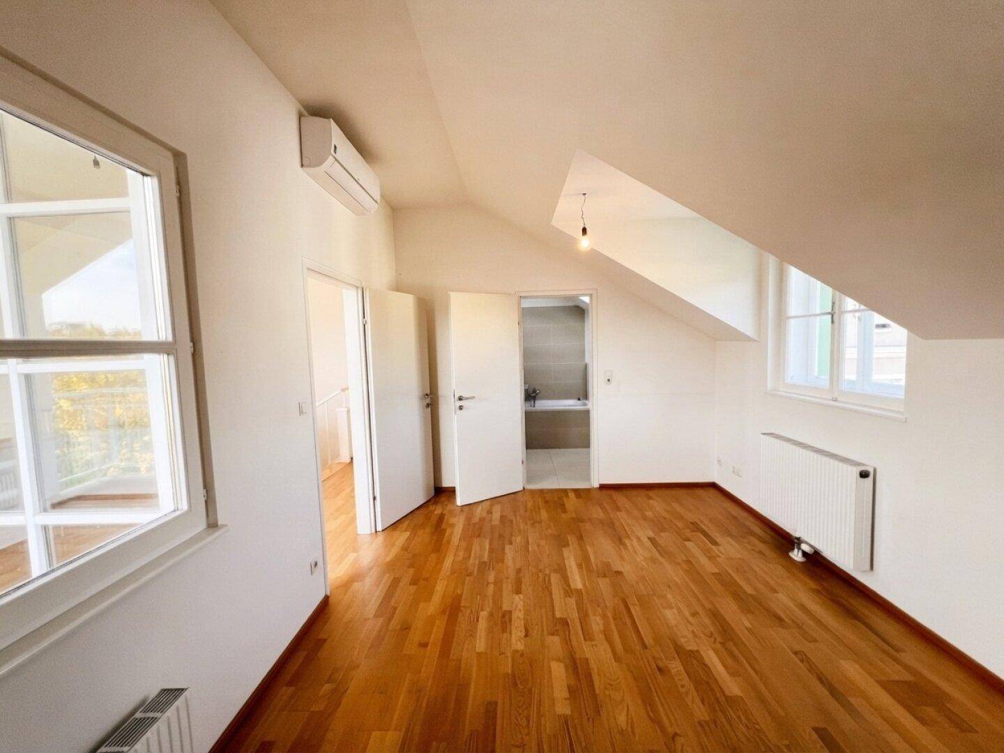 Geräumiges Schlafzimmer im Dachgeschoss mit Parkettboden und Zugang zum Bad.