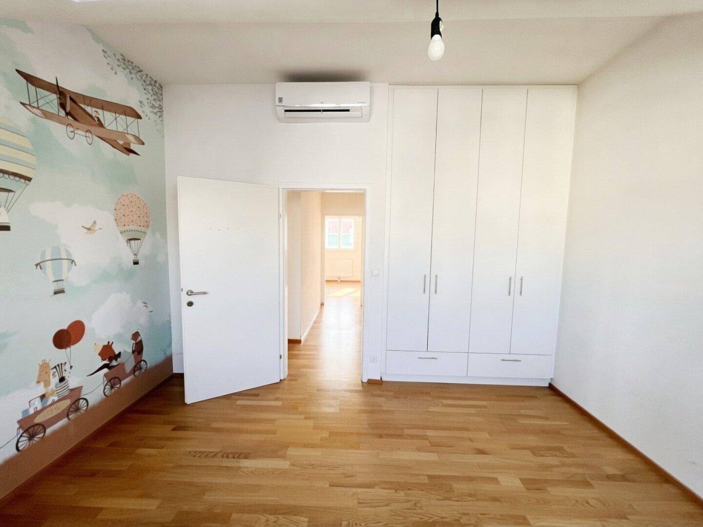 Kinderzimmer mit Einbauschränken, Holzboden und Klimaanlage, bereit zur individuellen Gestaltung.