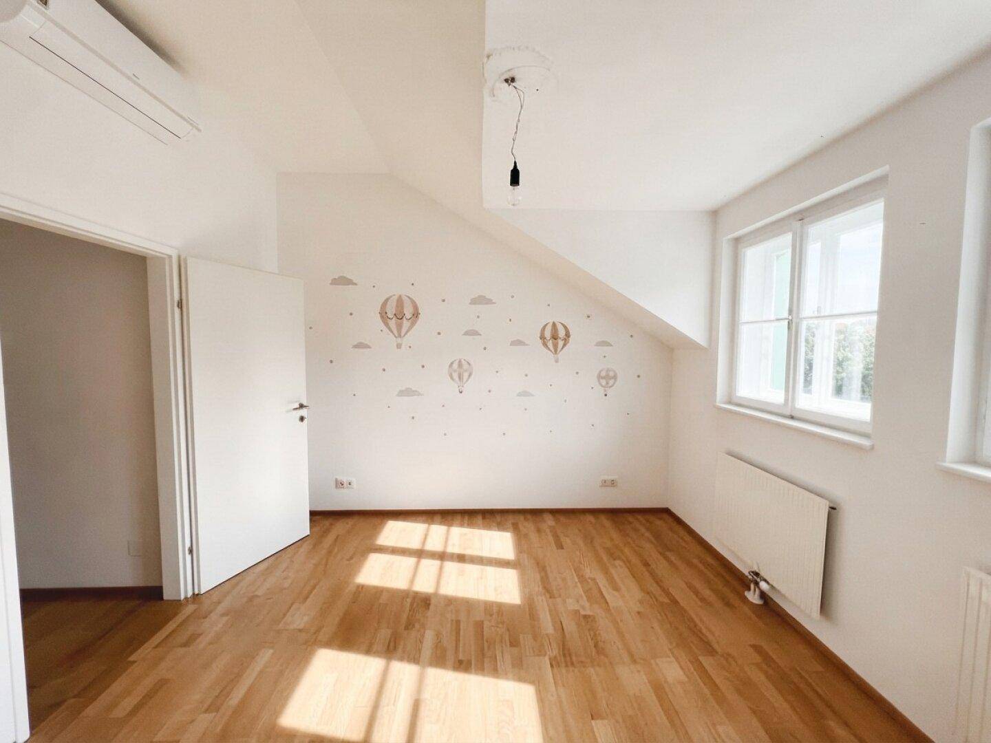 Helles Zimmer mit Holzboden, Dachschräge und Fenster, ideal als Kinder- oder Gästezimmer.