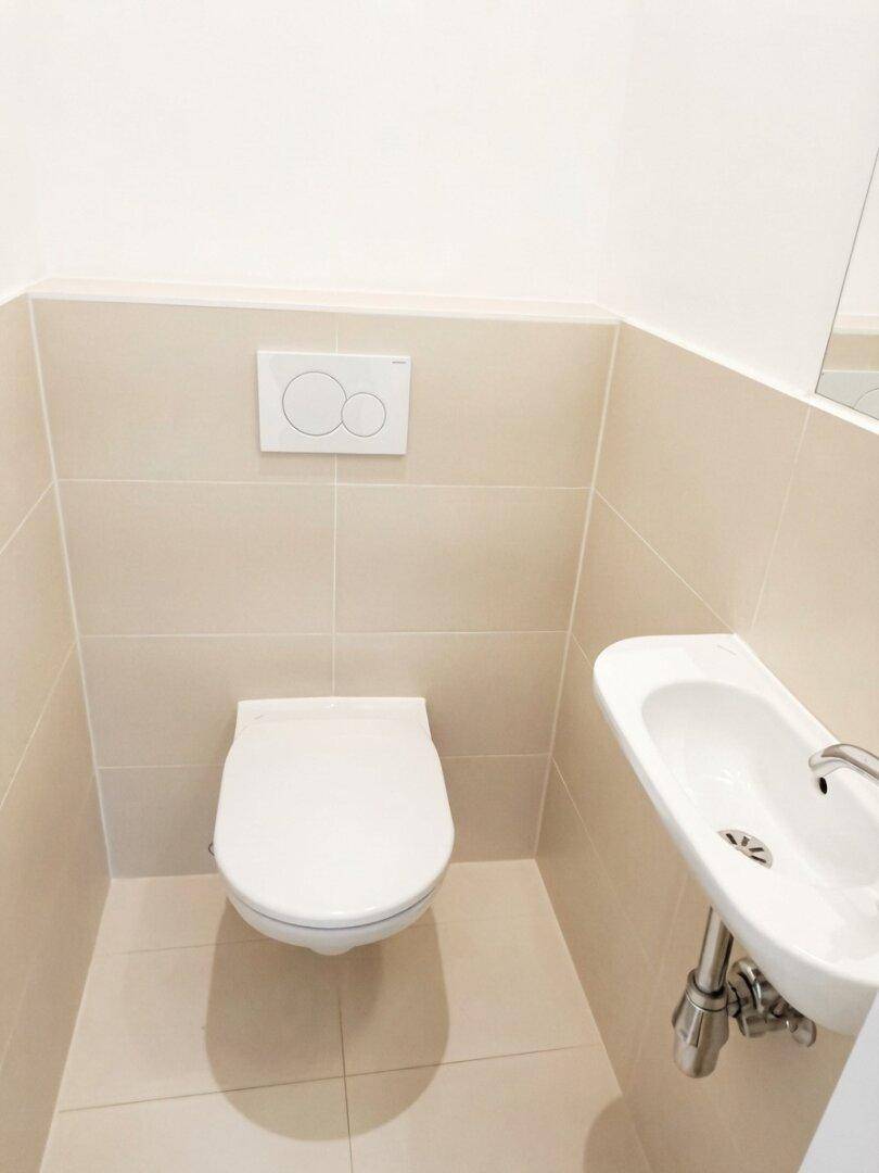 Separates Gäste-WC mit Wand-WC und kleinem Handwaschbecken, in neutralen Beigetönen gefliest.