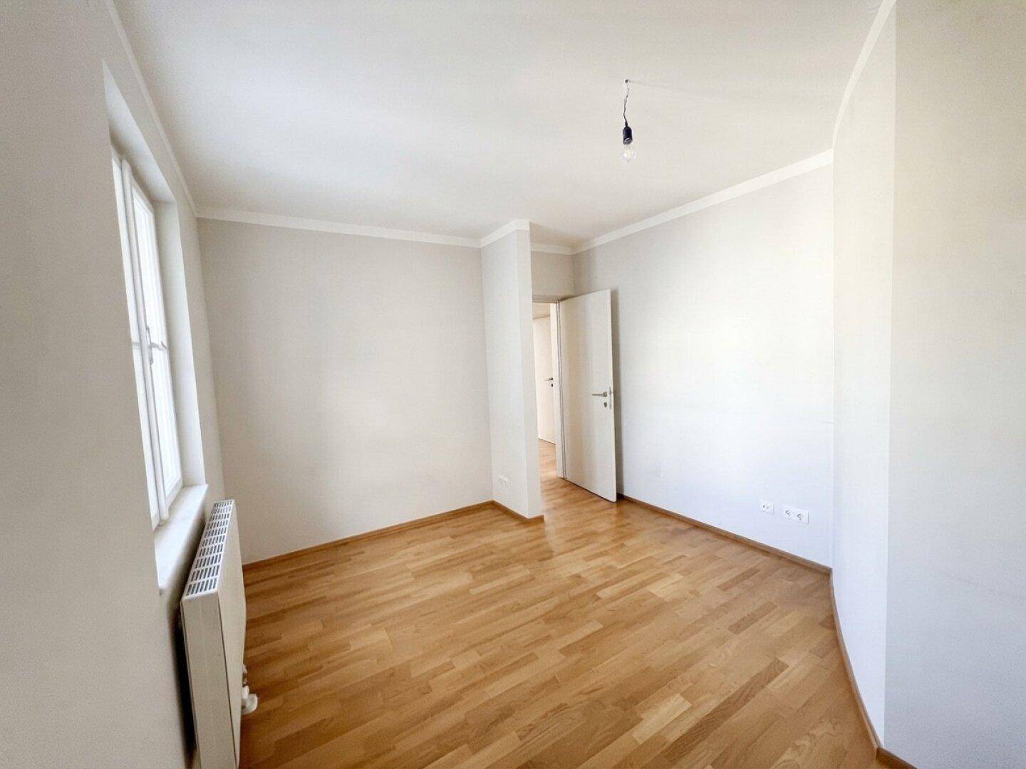 Helles, leeres Zimmer mit Parkettboden und weiß gestrichenen Wänden.