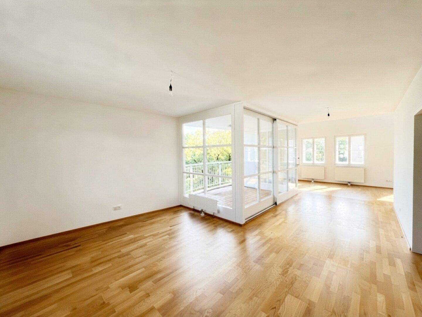 Heller, leerer Wohnbereich mit Parkettboden und Zugang zum Balkon.