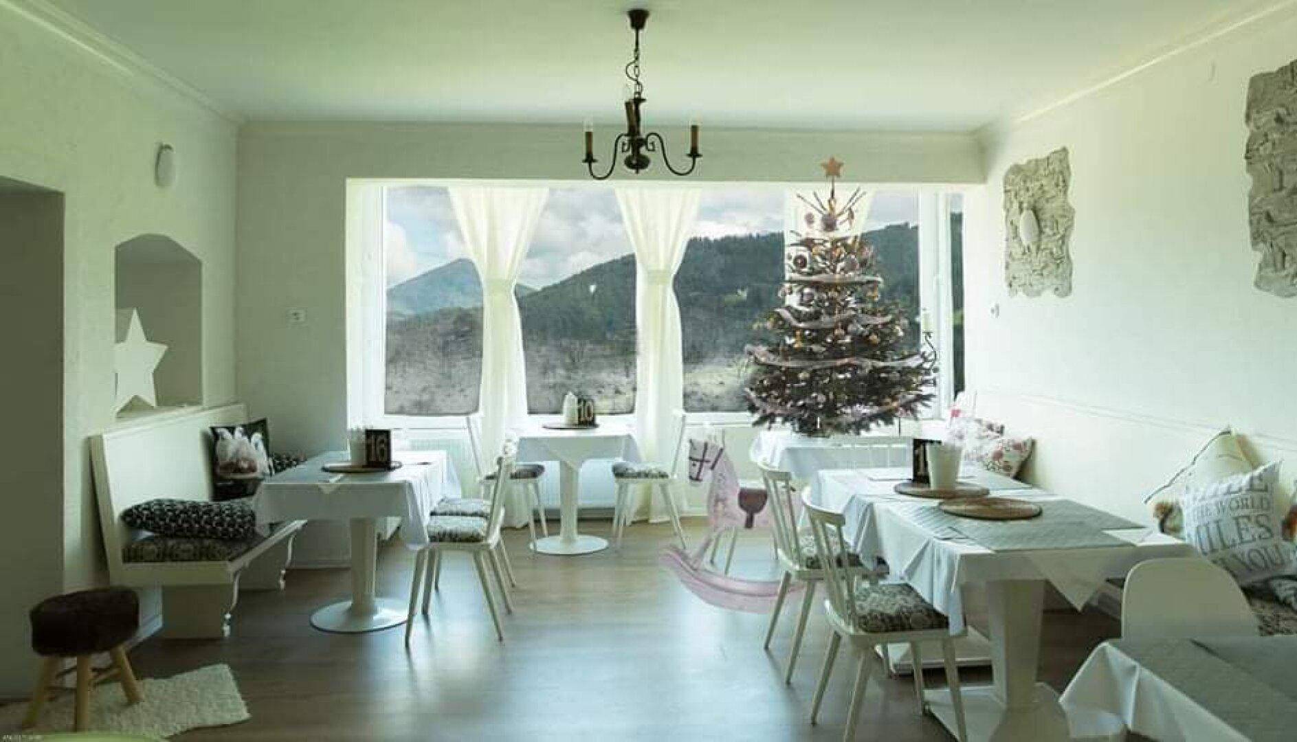 Gemütlicher Essbereich mit Holzboden, weißen Tischen und einem großen Fenster mit Blick auf die verschneiten Berge.