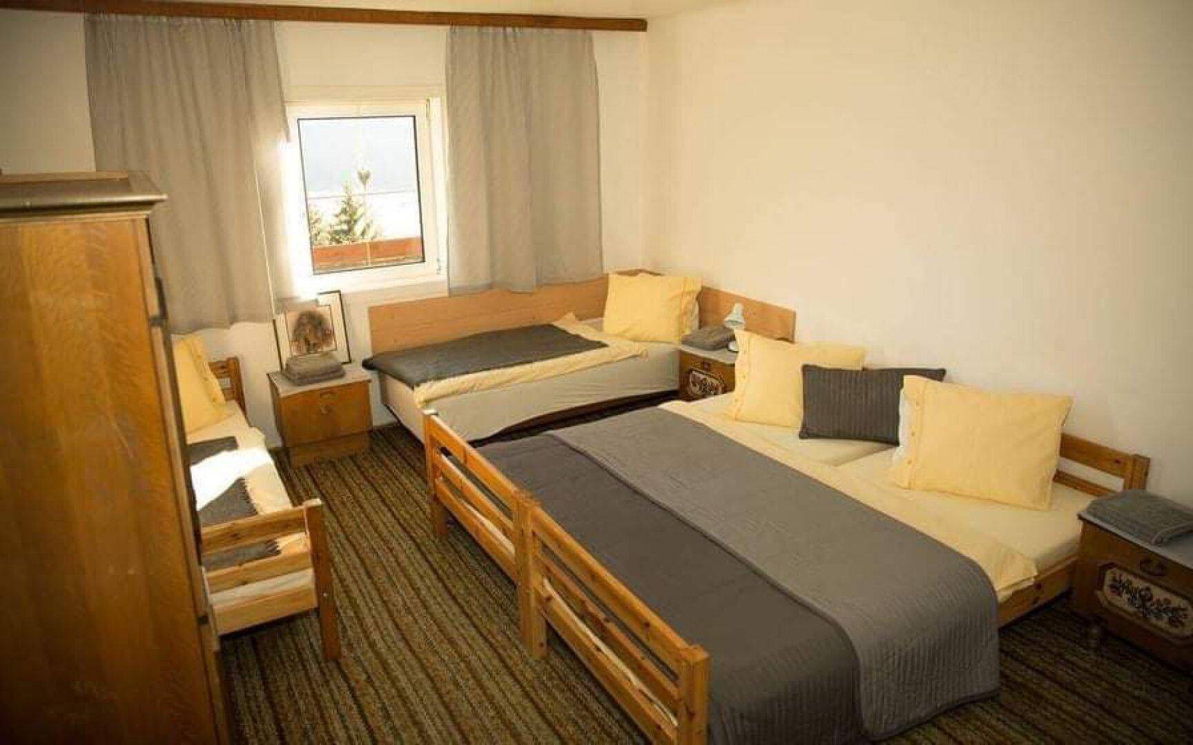 Einfaches Schlafzimmer mit mehreren Betten, Teppichboden und einem Fenster mit Blick auf die umliegende Landschaft.