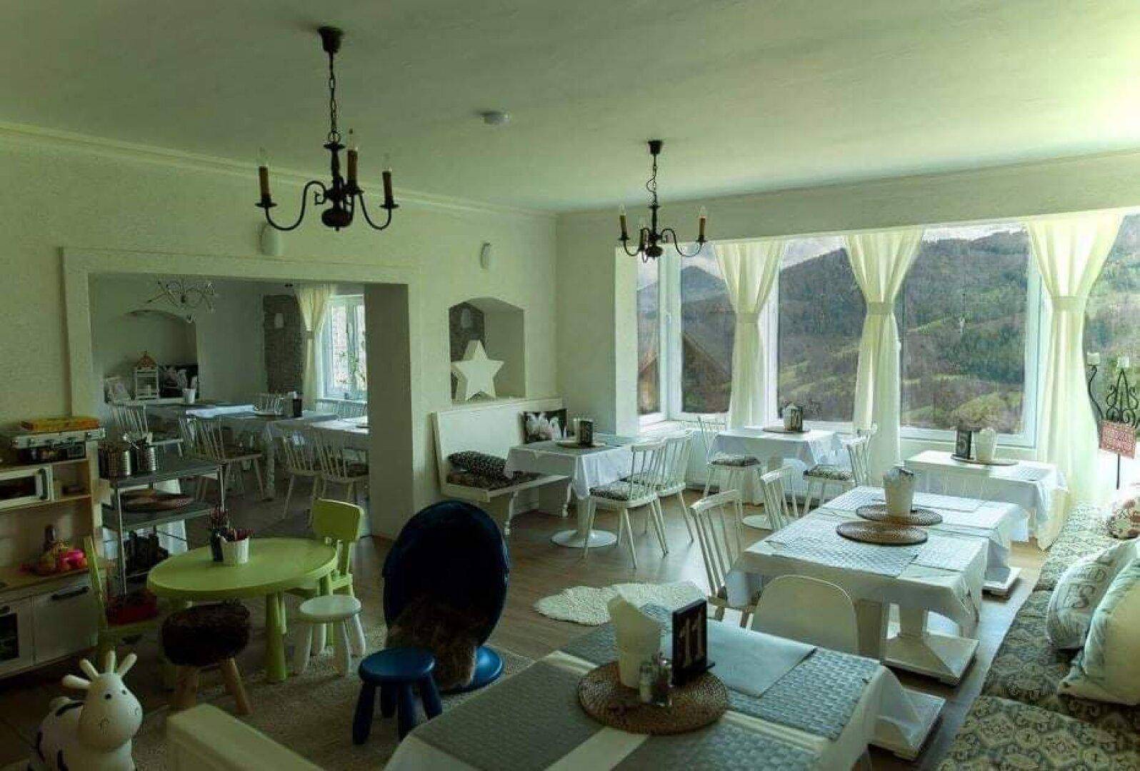 Geräumiger Essbereich mit Holzboden, vielen Tischen und einem Kinderbereich, der viel natürliches Licht erhält.