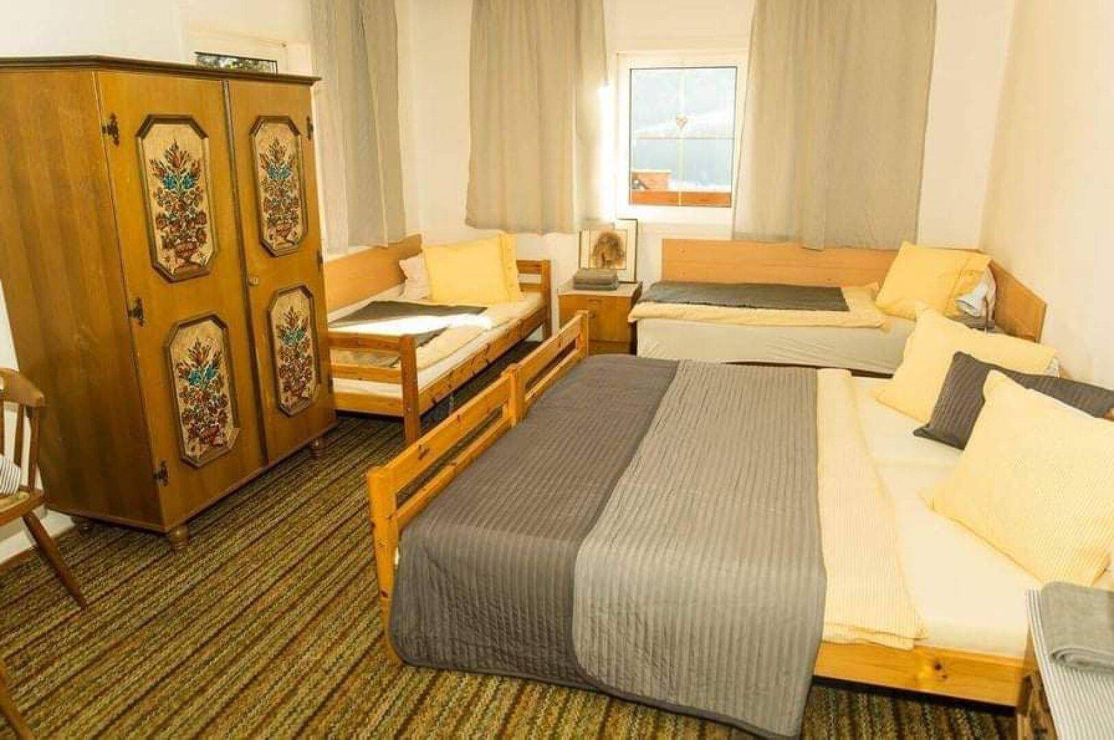 Traditionelles Schlafzimmer mit Holzmöbeln, Teppichboden und einem Fenster, das viel Tageslicht hereinlässt.