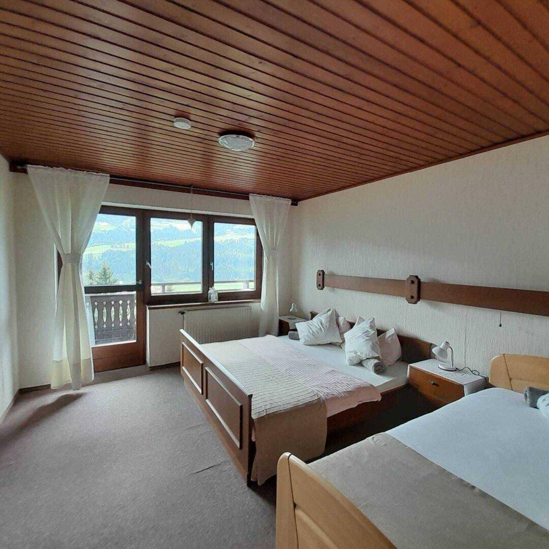 Helles Schlafzimmer mit Holzbalkendecke, Teppichboden und Zugang zu einem Balkon mit Bergblick.