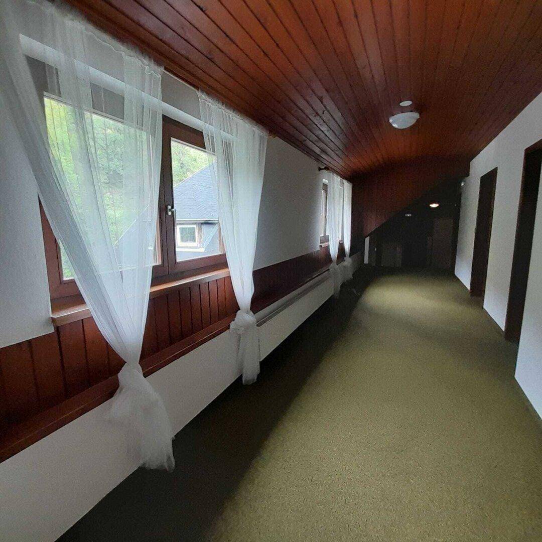 Langer Flur mit Teppichboden, Holzverkleidung und Fenstern, die den Raum mit natürlichem Licht erhellen.
