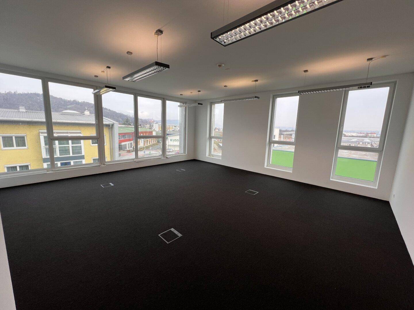 Geräumiges, helles Büro mit großen Fenstern, die einen weiten Blick auf die umliegende Bebauung ermöglichen.