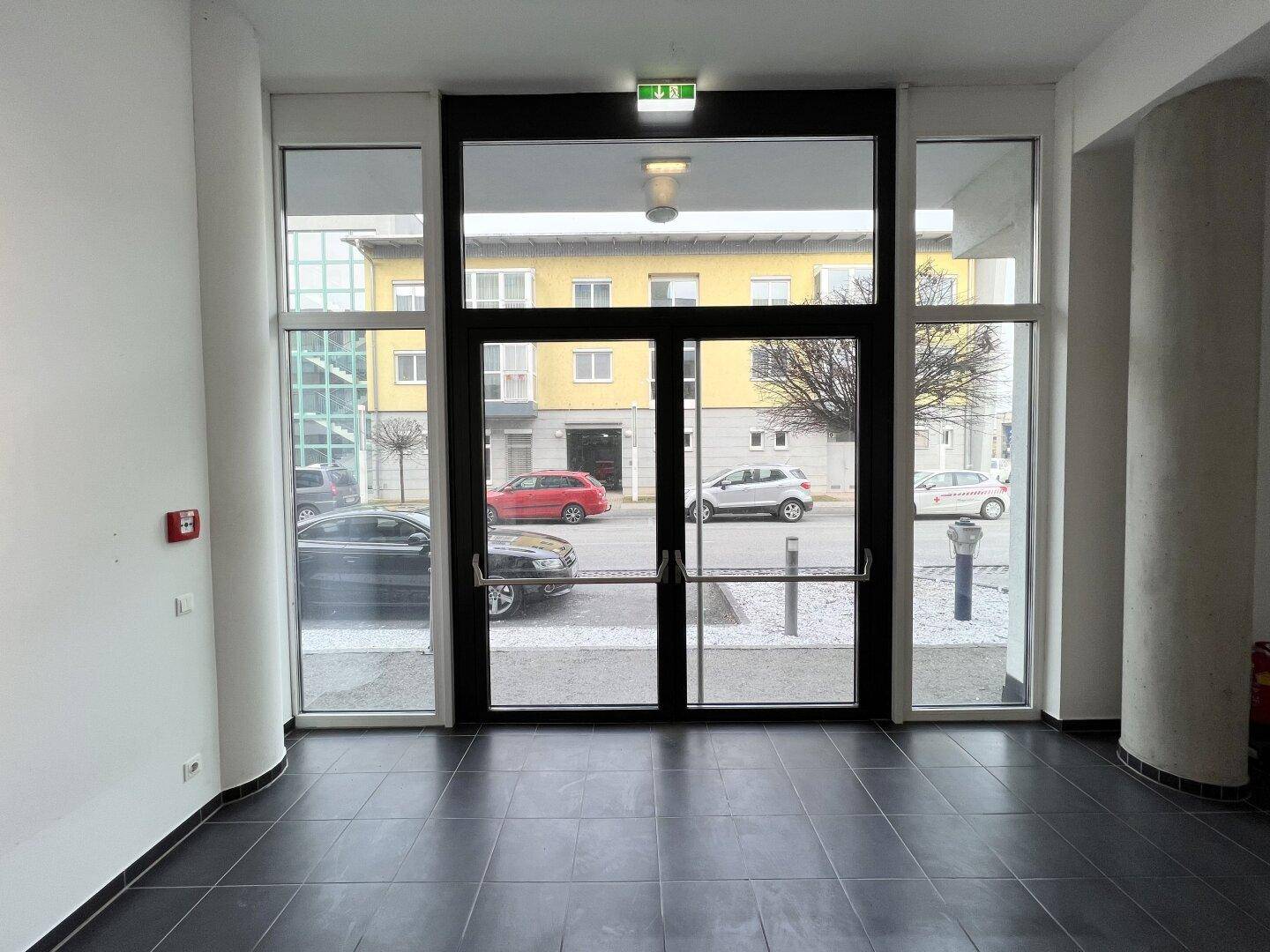 Heller Eingangsbereich eines Gewerberaums mit großen Glastüren und Blick auf die Straße.