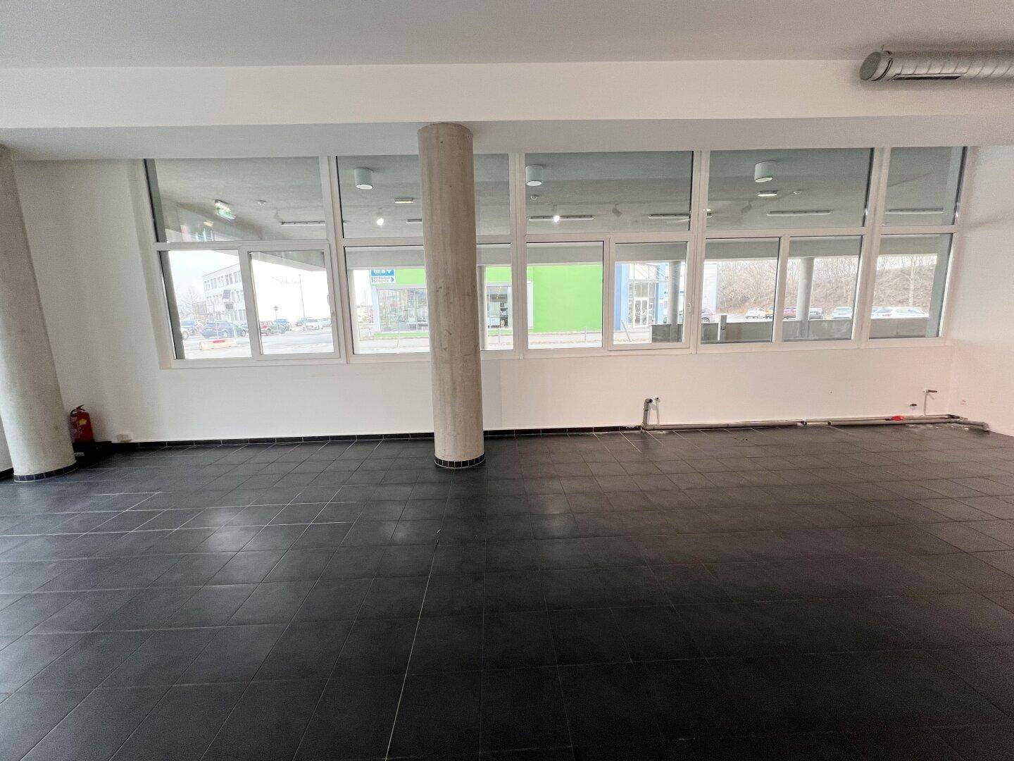 Große Fensterfront in einem Gewerberaum, die viel Tageslicht hereinlässt und einen Blick auf die Umgebung bietet.