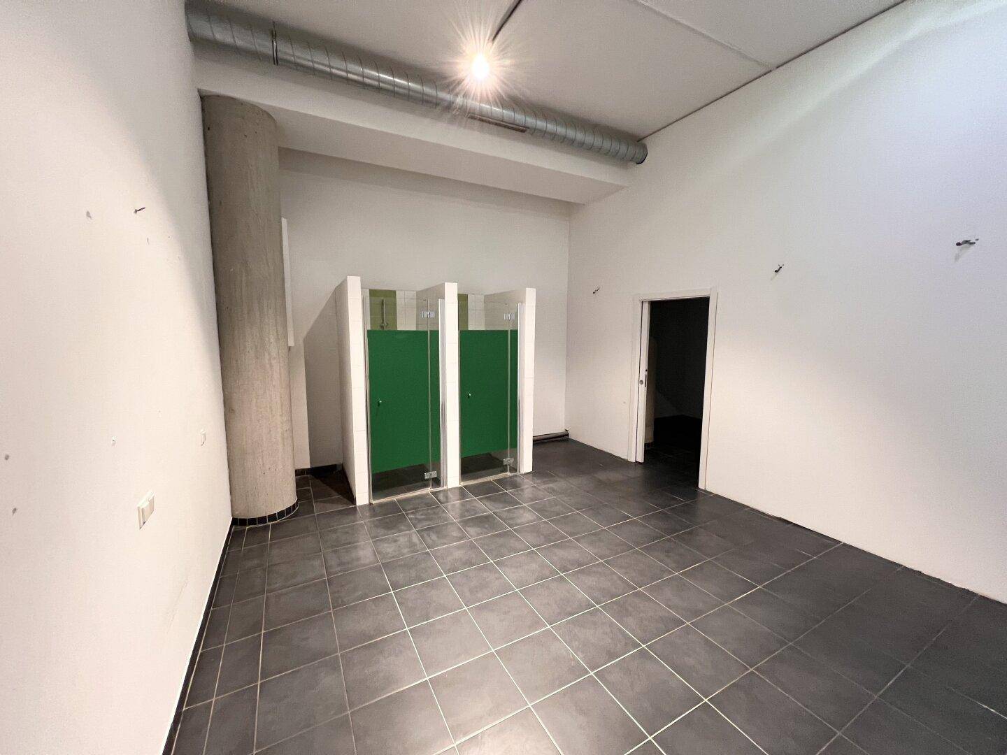Gewerberaum mit integrierten Duschkabinen und sichtbaren Lüftungsrohren an der Decke, bereit zur Nutzung.
