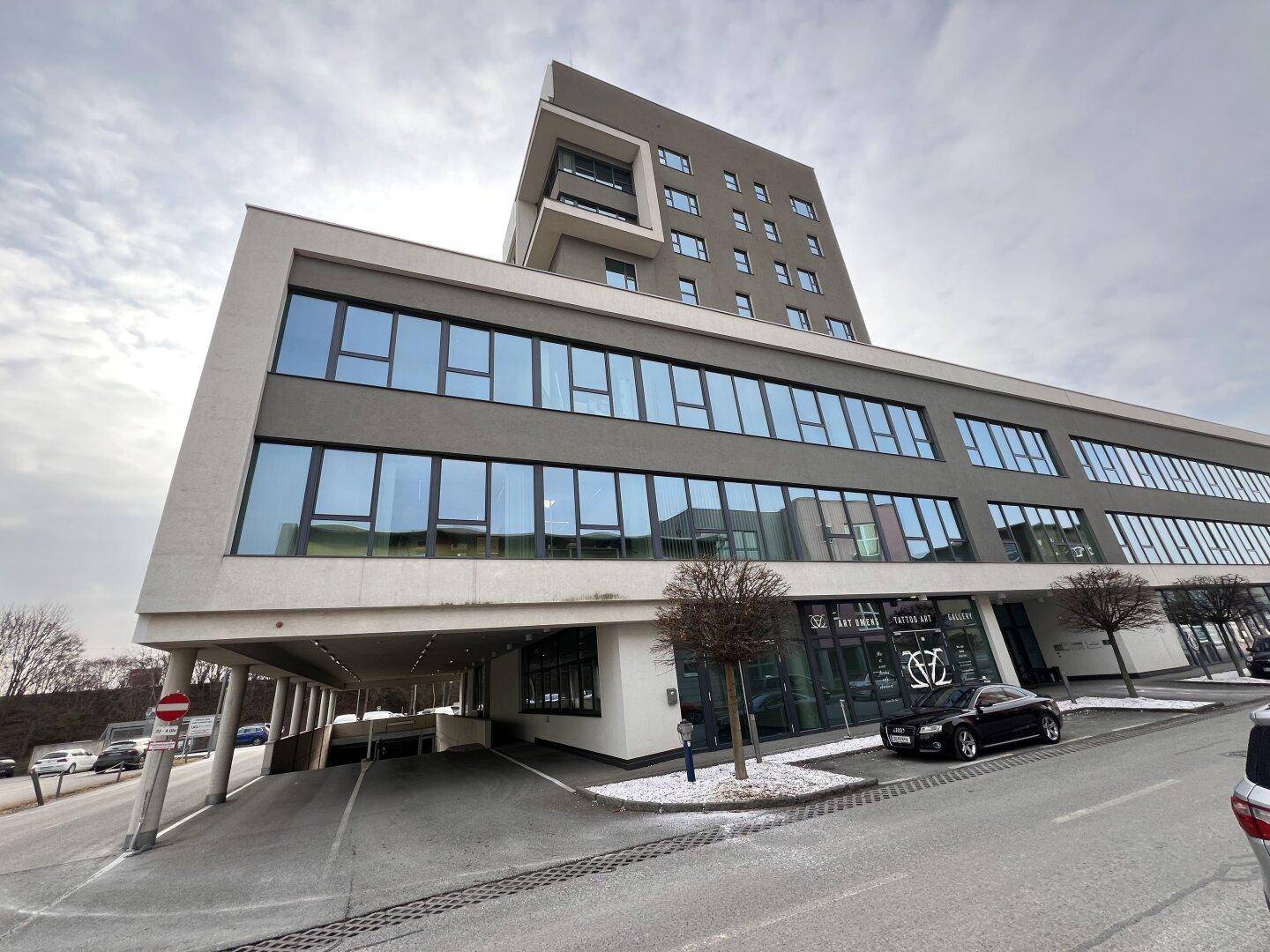 Modernes Geschäftsgebäude mit markanter Architektur, großen Glasflächen und überdachten Parkmöglichkeiten.