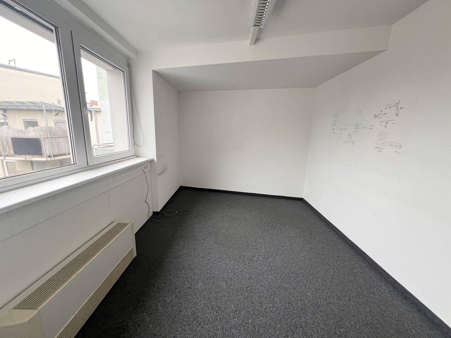 Leeres Büro mit Teppichboden, Fenster und einer Skizze an der weißen Wand.