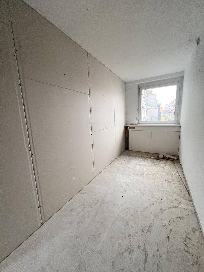 Büro im Rohbauzustand mit Trockenbauwänden, unfertigem Boden und einem Fenster.