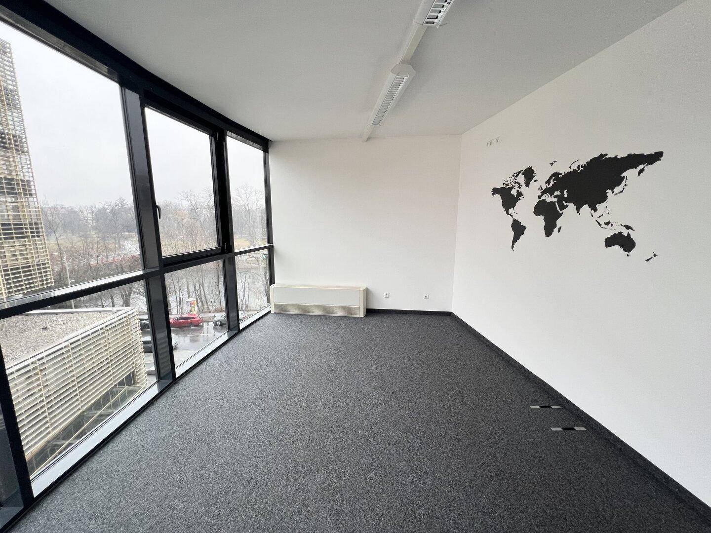 Geräumiges, leeres Büro mit Teppichboden, großen Fenstern und einer Weltkarte an der Wand.