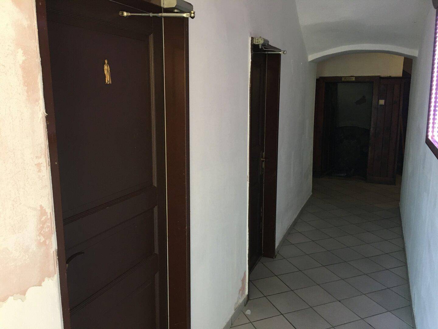 Langer Flur mit Fliesenboden und mehreren Holztüren, der zu verschiedenen Räumen führt.