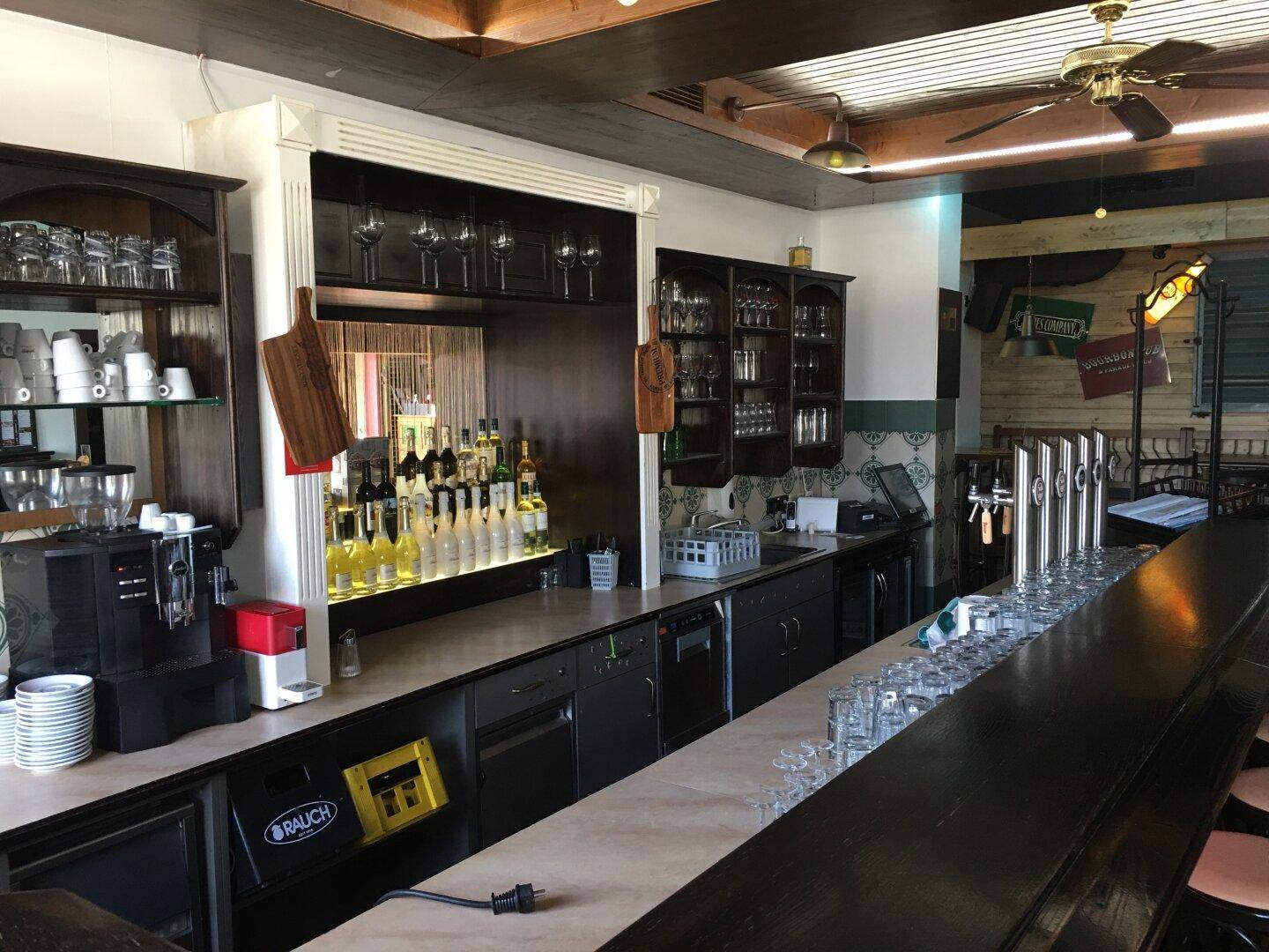 Detailansicht einer gut ausgestatteten Bar mit Zapfanlage, Kaffeemaschine und vielen Gläsern.