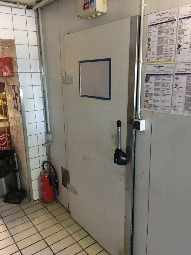 Große Kühlraumtür in einer Gewerbeküche mit Fliesenwänden und Feuerlöscher.