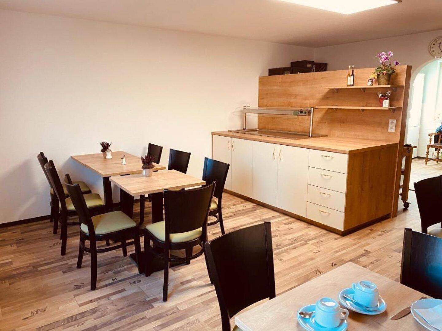 Heller Frühstücksraum mit Holztischen, Stühlen und einem Buffetbereich mit Holzverkleidung.