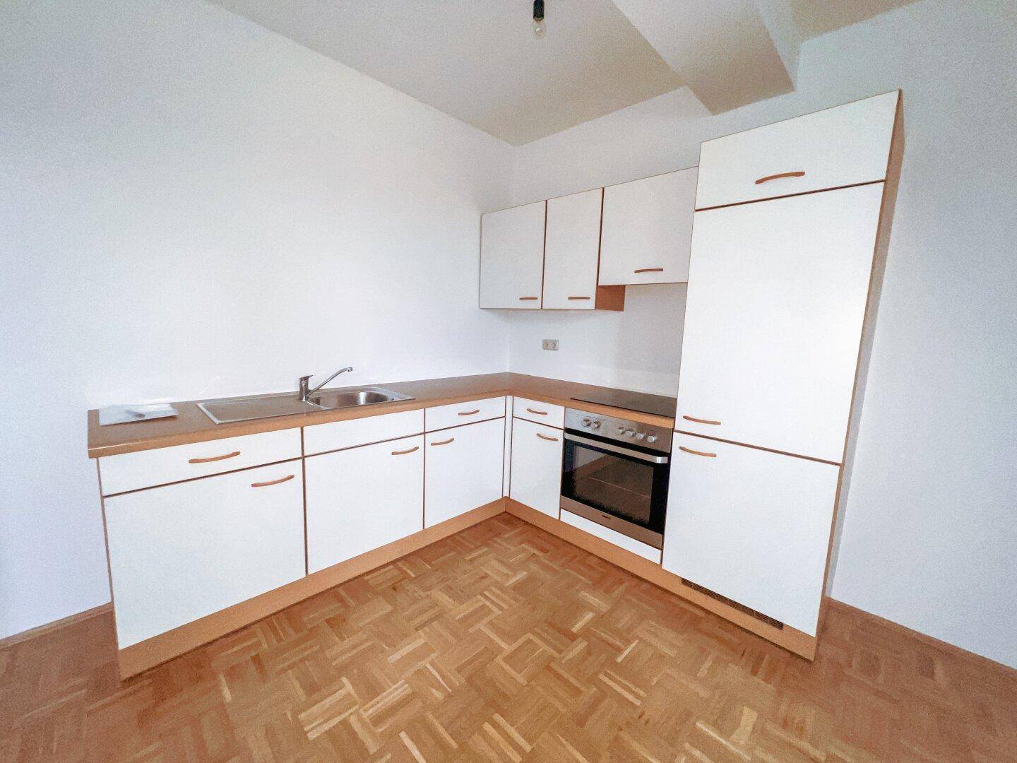 Funktionale Küchenzeile mit weißen Schränken, Holz-Arbeitsplatte und integriertem Backofen.