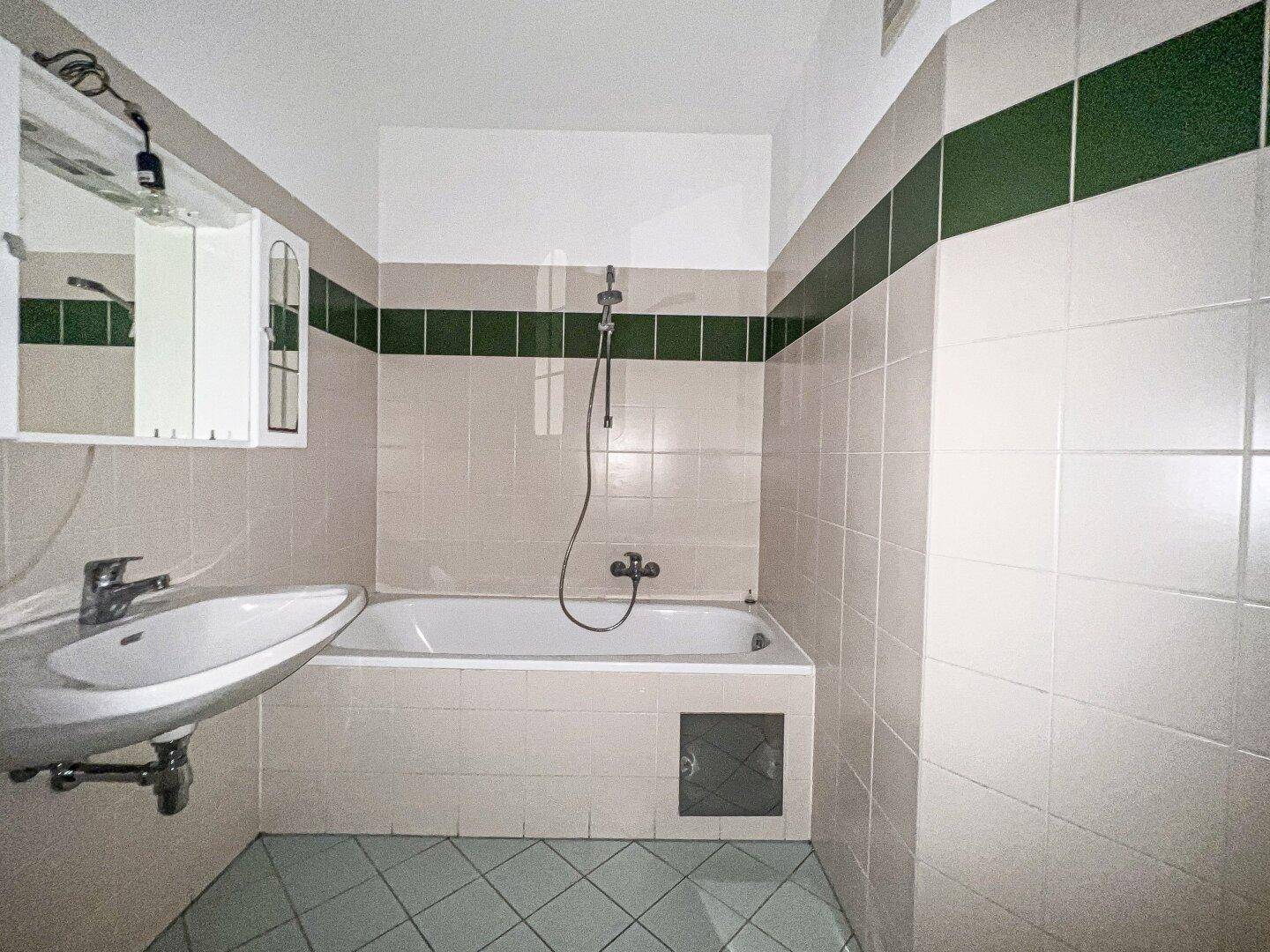 Badezimmer mit Badewanne, Waschbecken und Fliesen in Beige und Dunkelgrün.