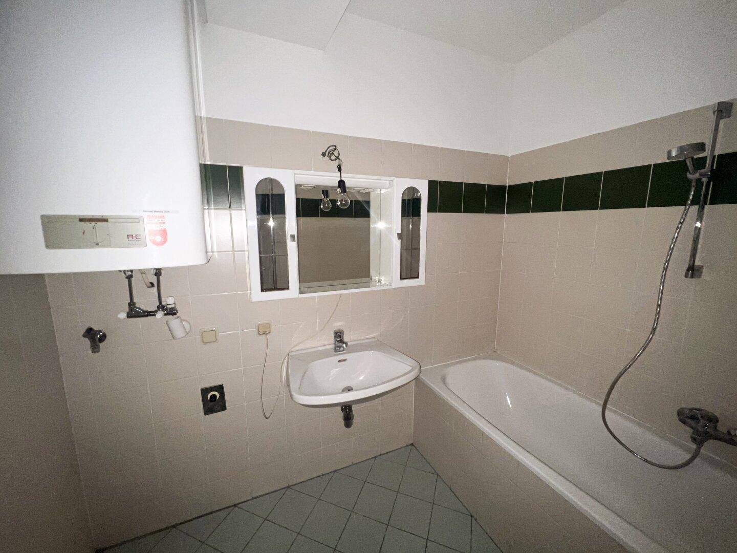Badezimmer mit Badewanne, Waschbecken, Boiler und Fliesen im Stil der 80er Jahre.