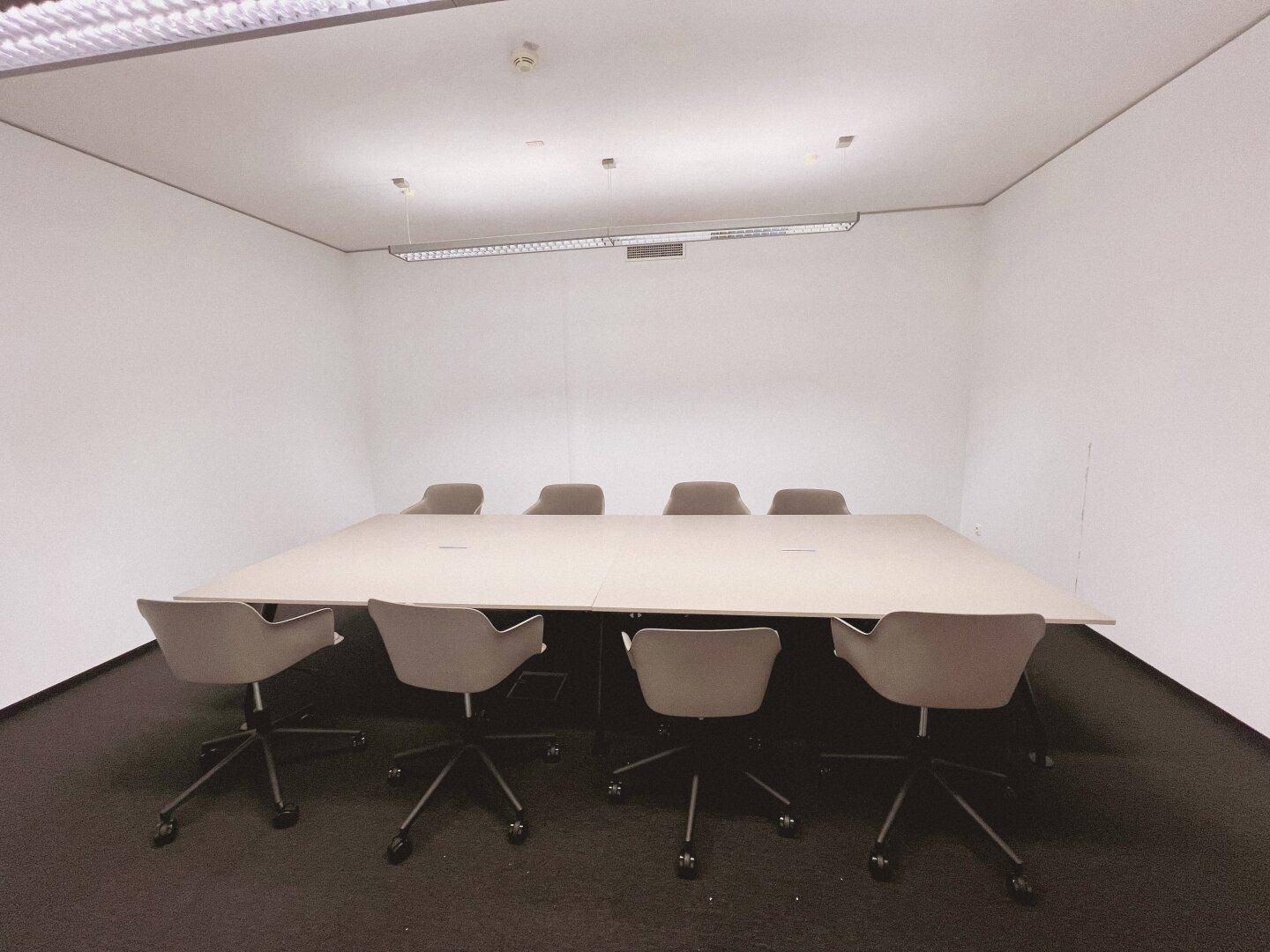 Heller Konferenzraum mit großem Besprechungstisch und bequemen Stühlen, ausgestattet für produktive Arbeit.