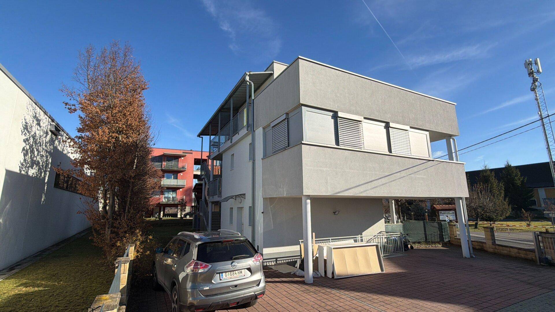 Seitenansicht des modernen Gebäudes mit Parkplatz und einem Auto unter strahlend blauem Himmel.