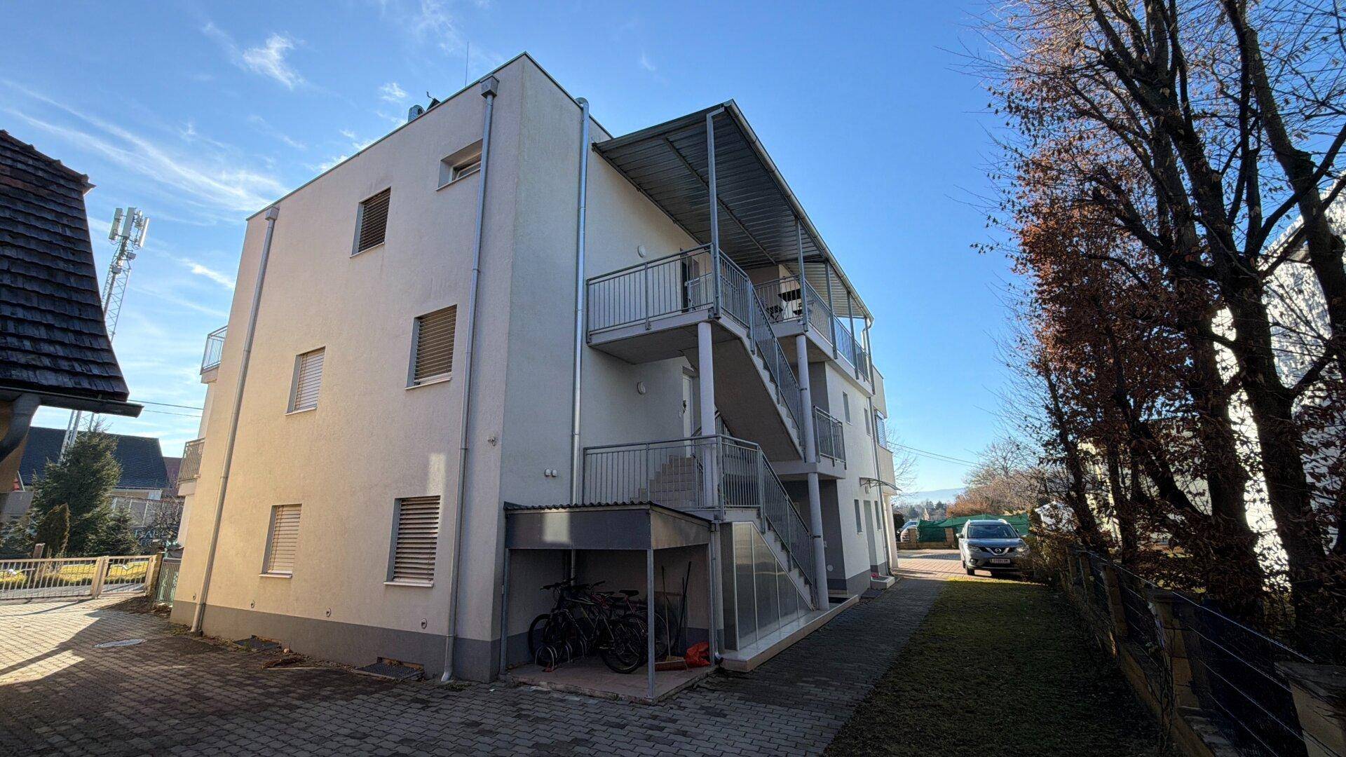 Seitenansicht des Mehrfamilienhauses mit Außentreppe, Balkonen und Fahrradabstellplatz.