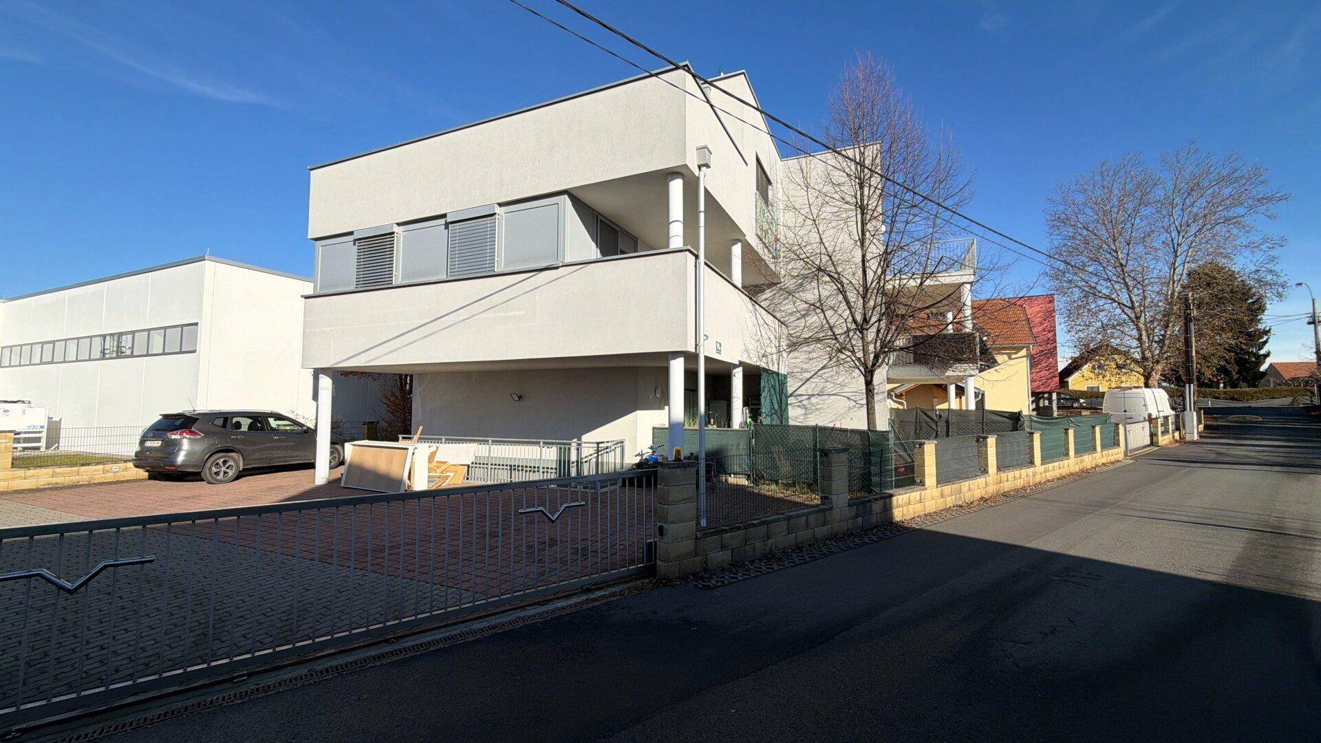Modernes Wohngebäude mit weißer Fassade und Rollläden, von der Straße aus gesehen.