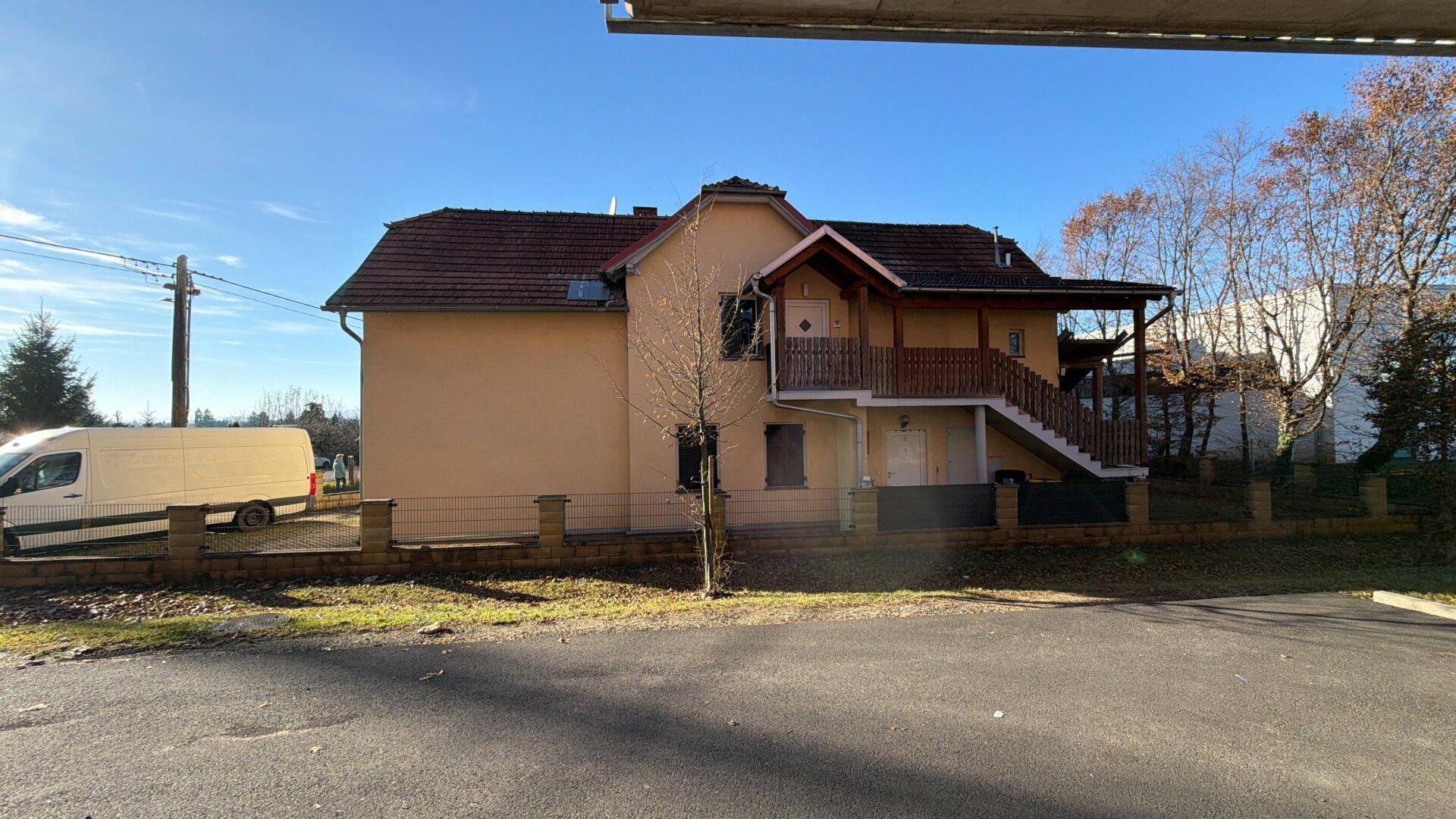 Seitenansicht des gelben Hauses mit überdachtem Eingang und Außentreppe unter blauem Himmel.