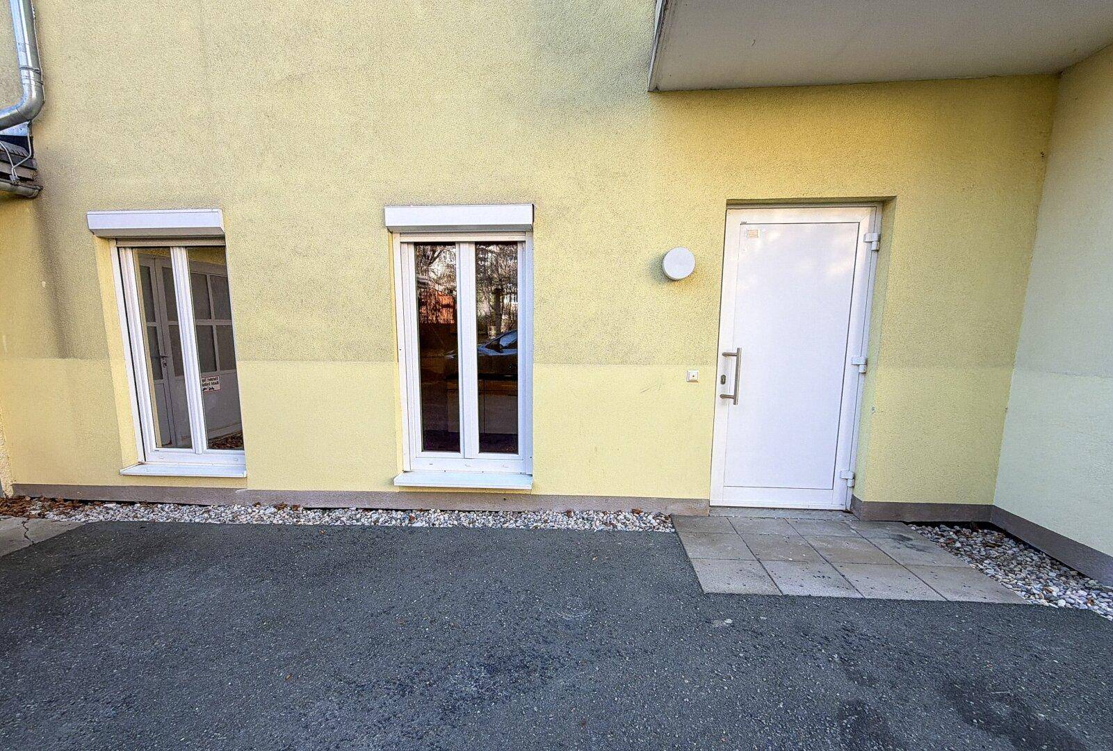 Gelb gestrichene Fassade mit zwei Fenstern und einer Eingangstür, ausgestattet mit Rollläden.