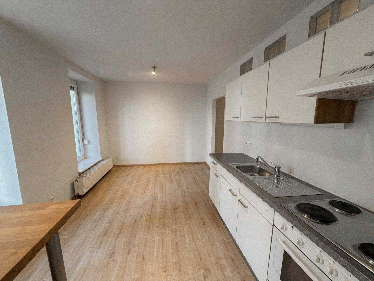Offener Küchenbereich mit Laminatboden und Blick auf den Wohnbereich mit Fenster.